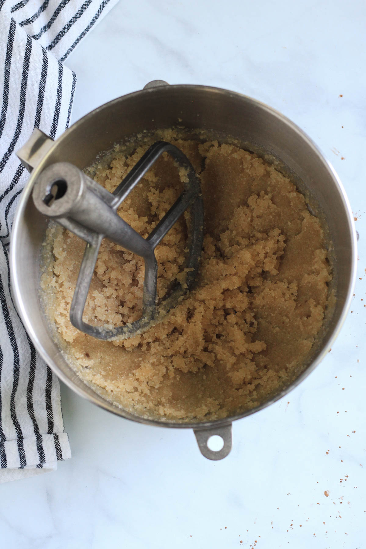 A silver mixing bowl with the paddle attachment and creamed oil and sugar.