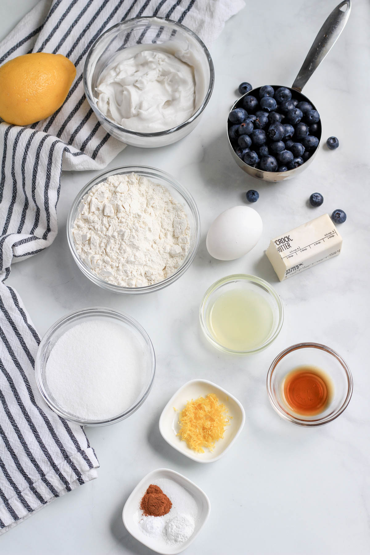Ingredients for lemon blueberry coffee cake on a white counter with a blue and white striped dish towel.