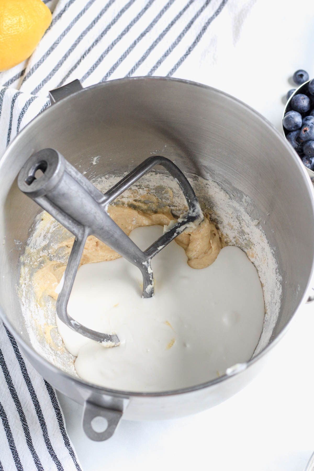 Coconut milk mixed with lemon juice added to the mixing bowl with a paddle attachment to the top left of the bowl.