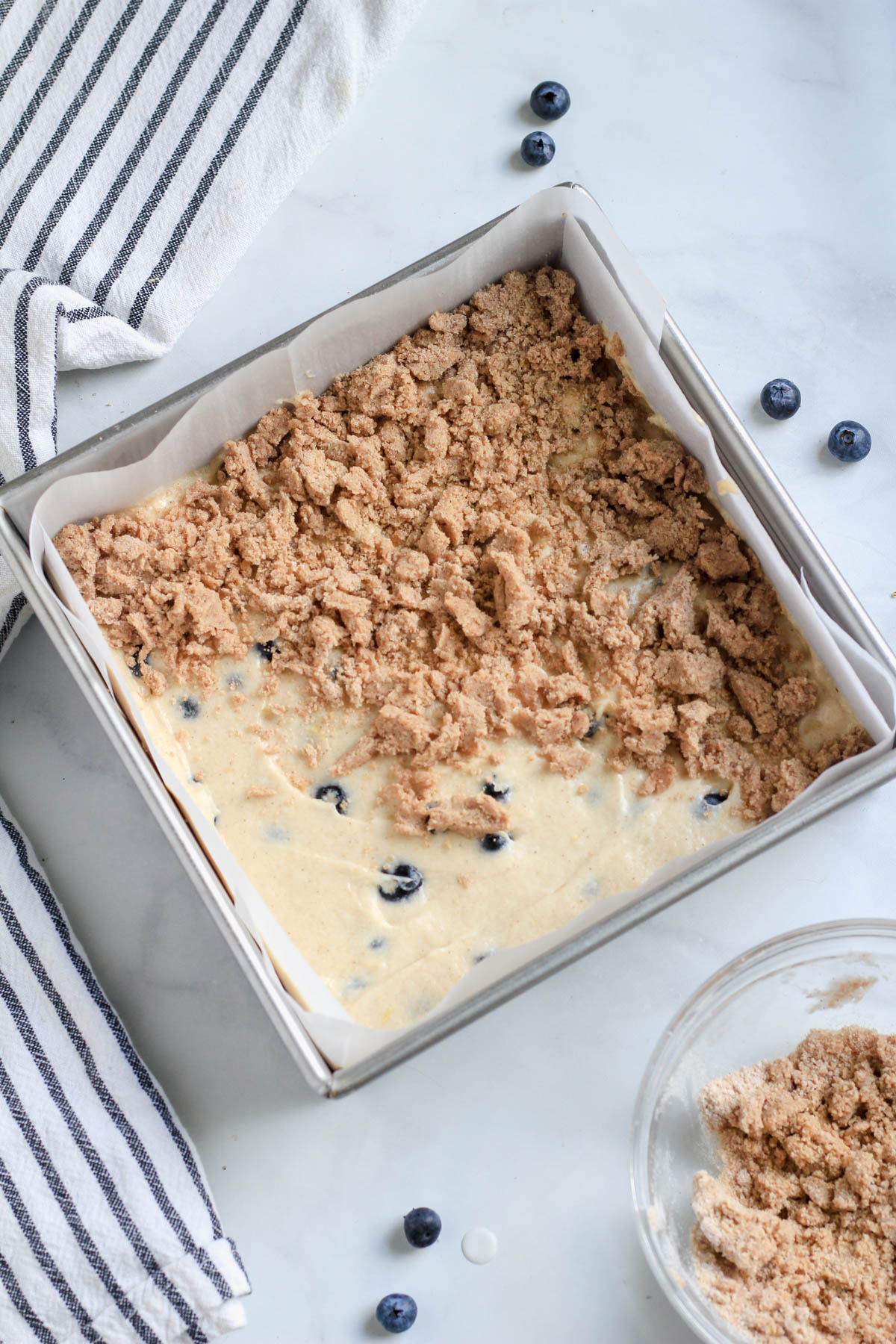 Lemon blueberry coffee cake in a square baking pan with half of the batter topped with the crumble before baking.
