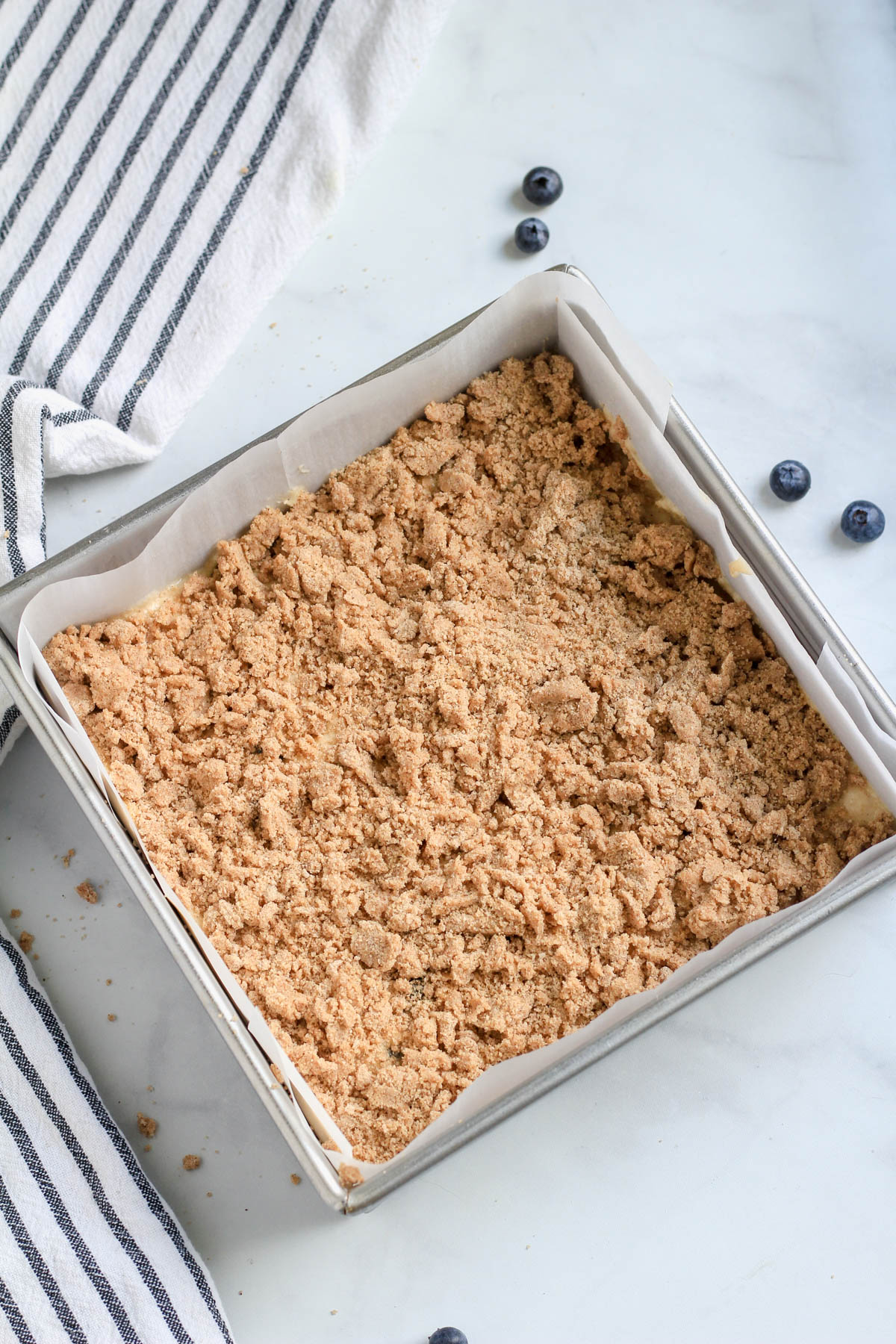 Lemon blueberry coffee cake in a silver baking pan topped with the crumble topping before baking.