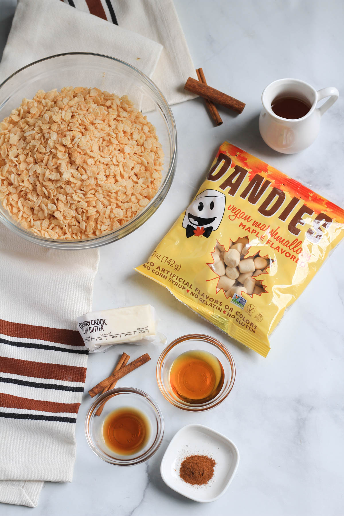 Ingredients for Maple Rice Krispie Treats on a white counter with cinnamon sticks.