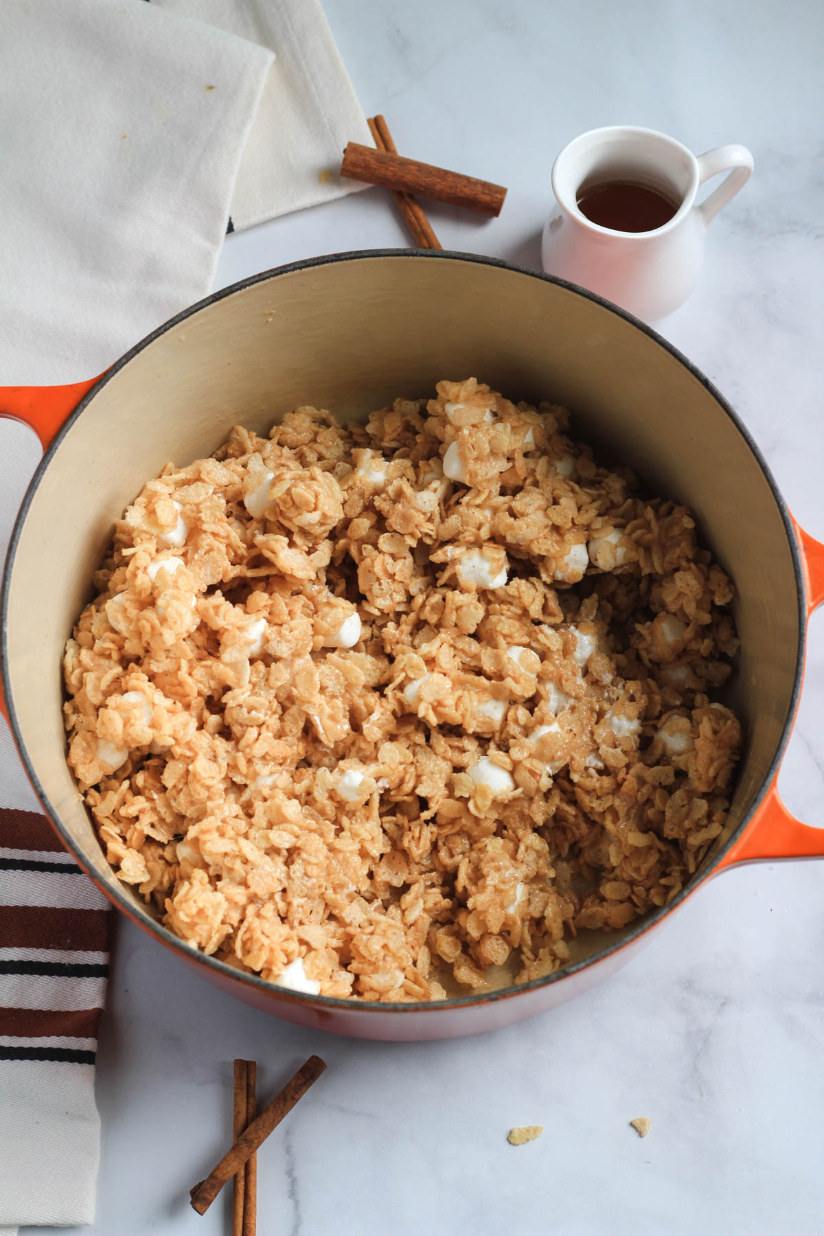 Maple Rice Krispies in an orange pot with a small jug of maple syrup in the back.