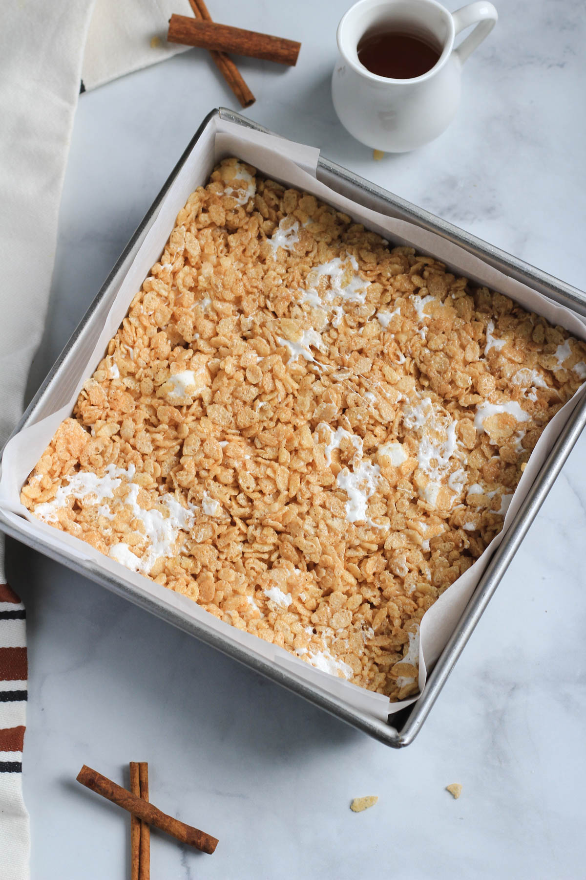 A square baking pan lined with parchment paper with maple Rice Krispie treats pressed into the pan.