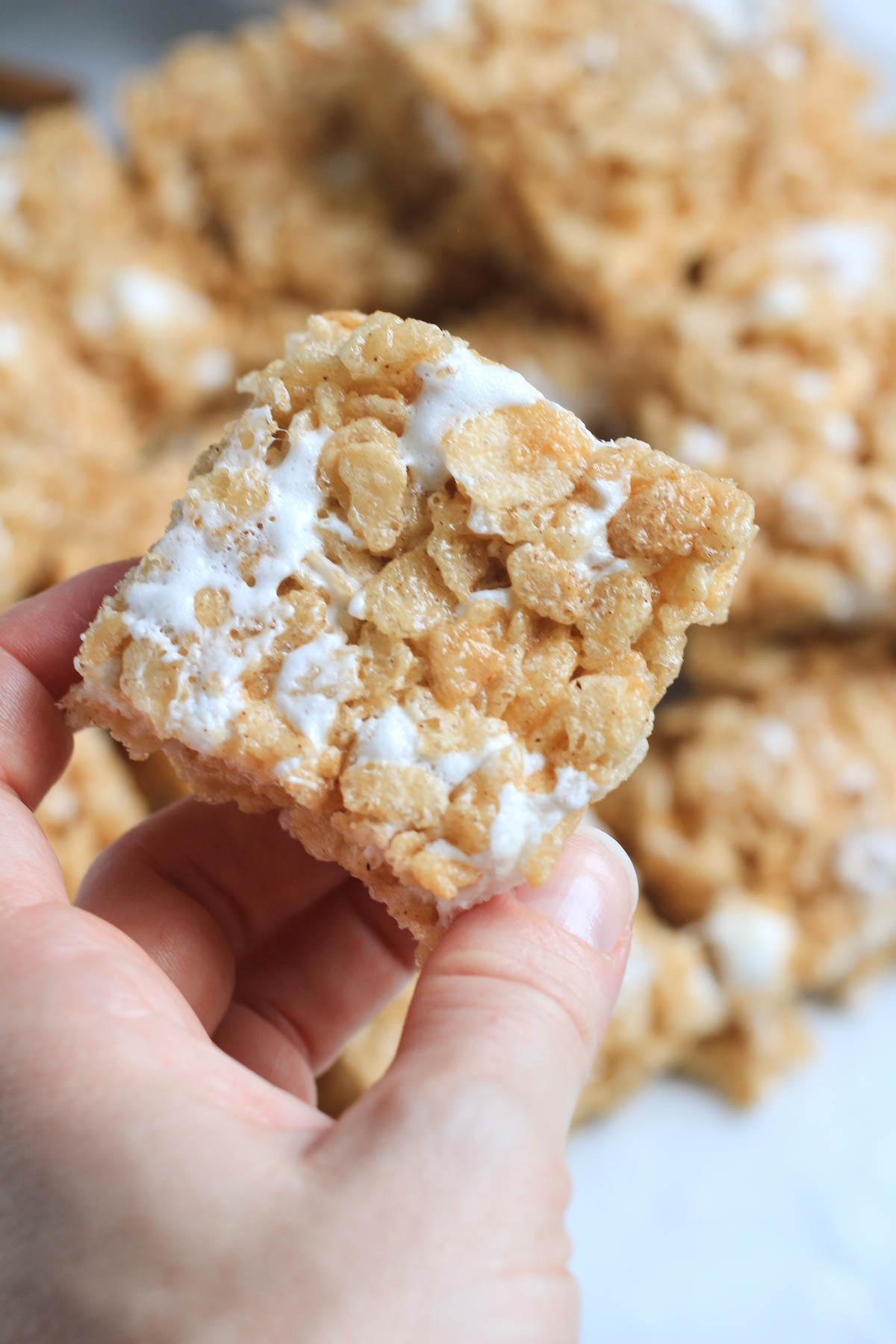 A hand holding a cinnamon maple Rice Krispie treat in front of a pile of treats.
