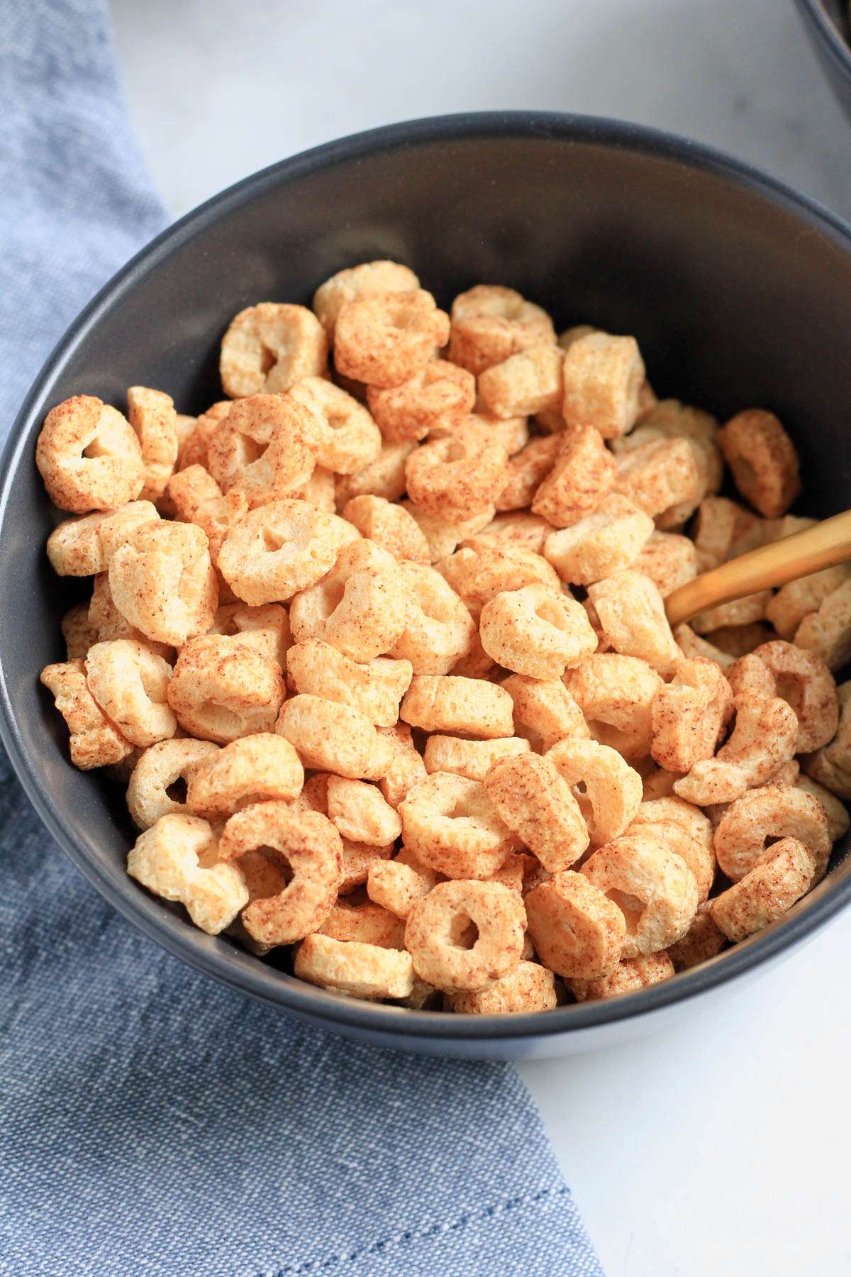A blue bowl of cinnamon cereal with a gold spoon on the right side and a blue towel on the left side.