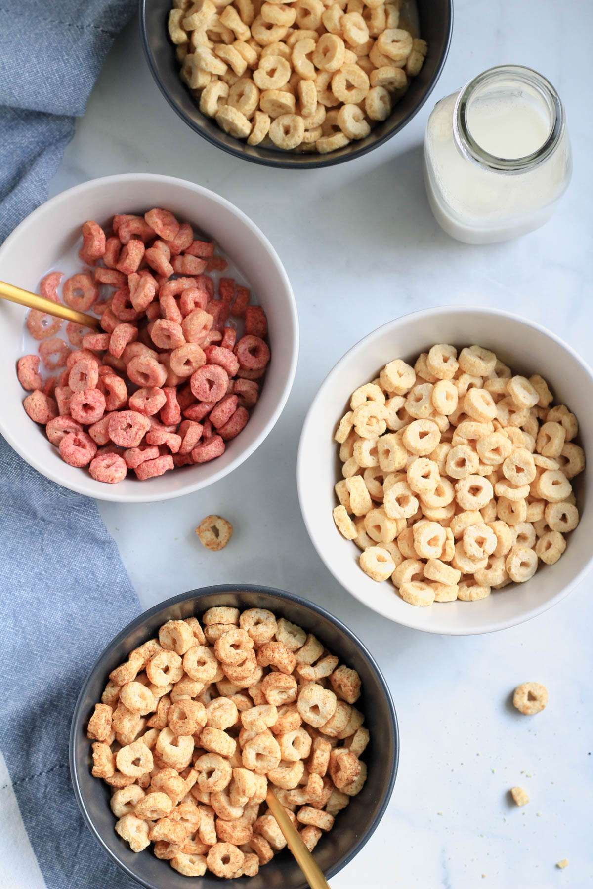 Four bowls of cereal on a white counter with a small jug of oat milk to the right.