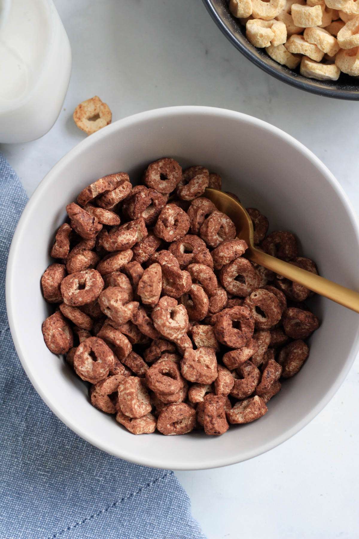 A white bowl with cocoa cereal and a gold spoon on the right side of the bowl.