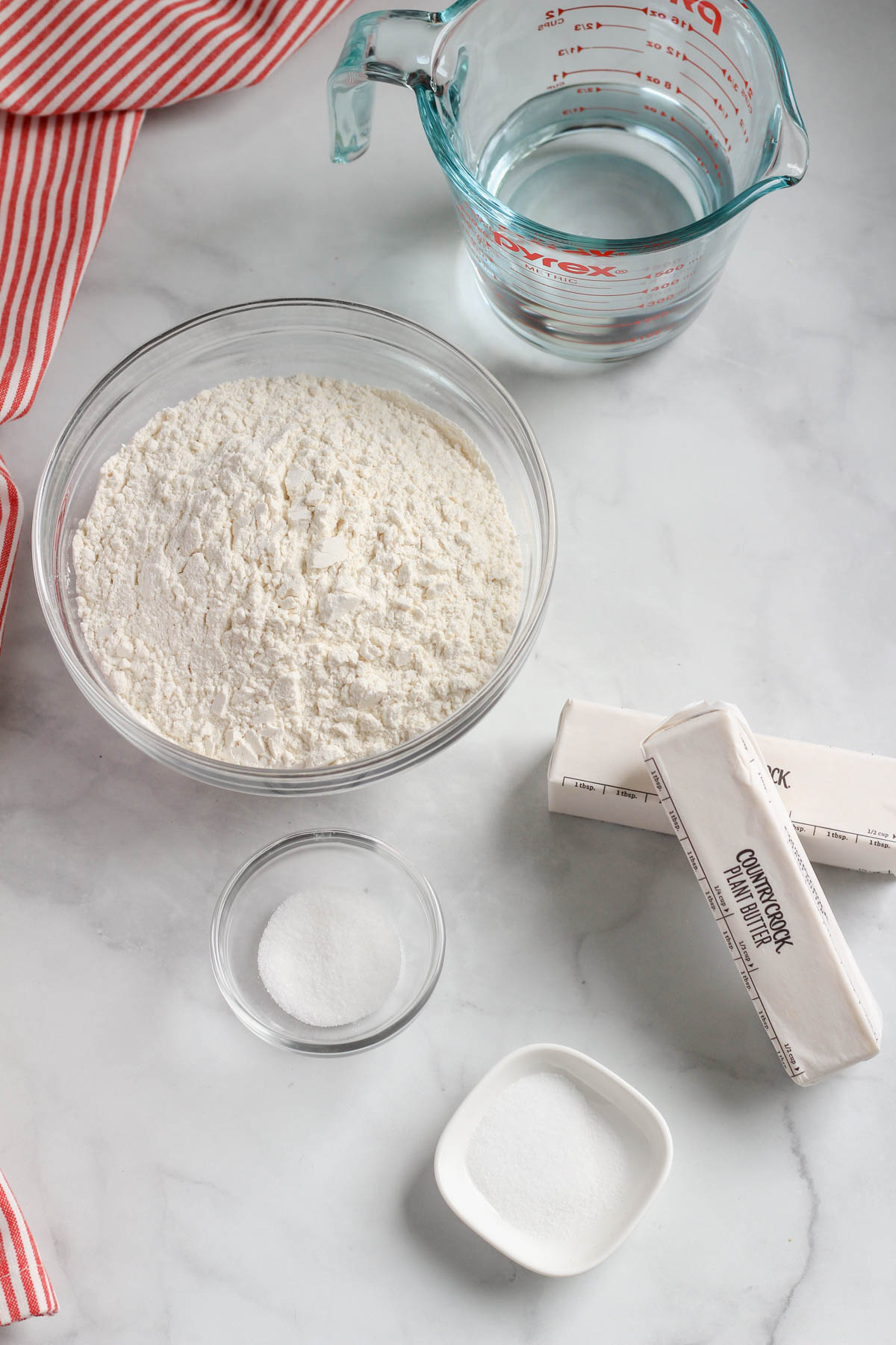Ingredients for a vegan all butter pie crust on a white counter with a red and white striped dish towel to the left.