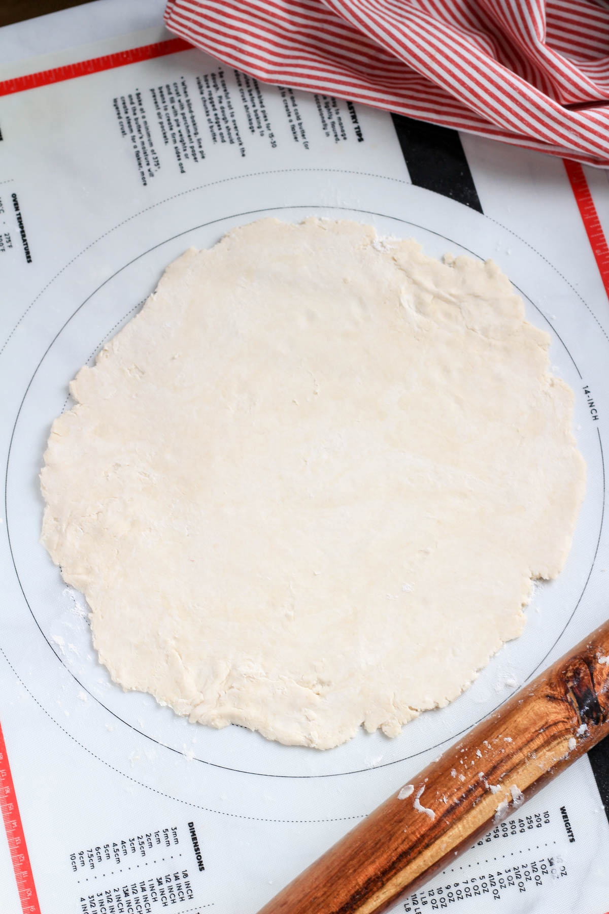 A pastry mat with a wooden rolling pin in the bottom right with a vegan all butter pie crust rolled on the mat.