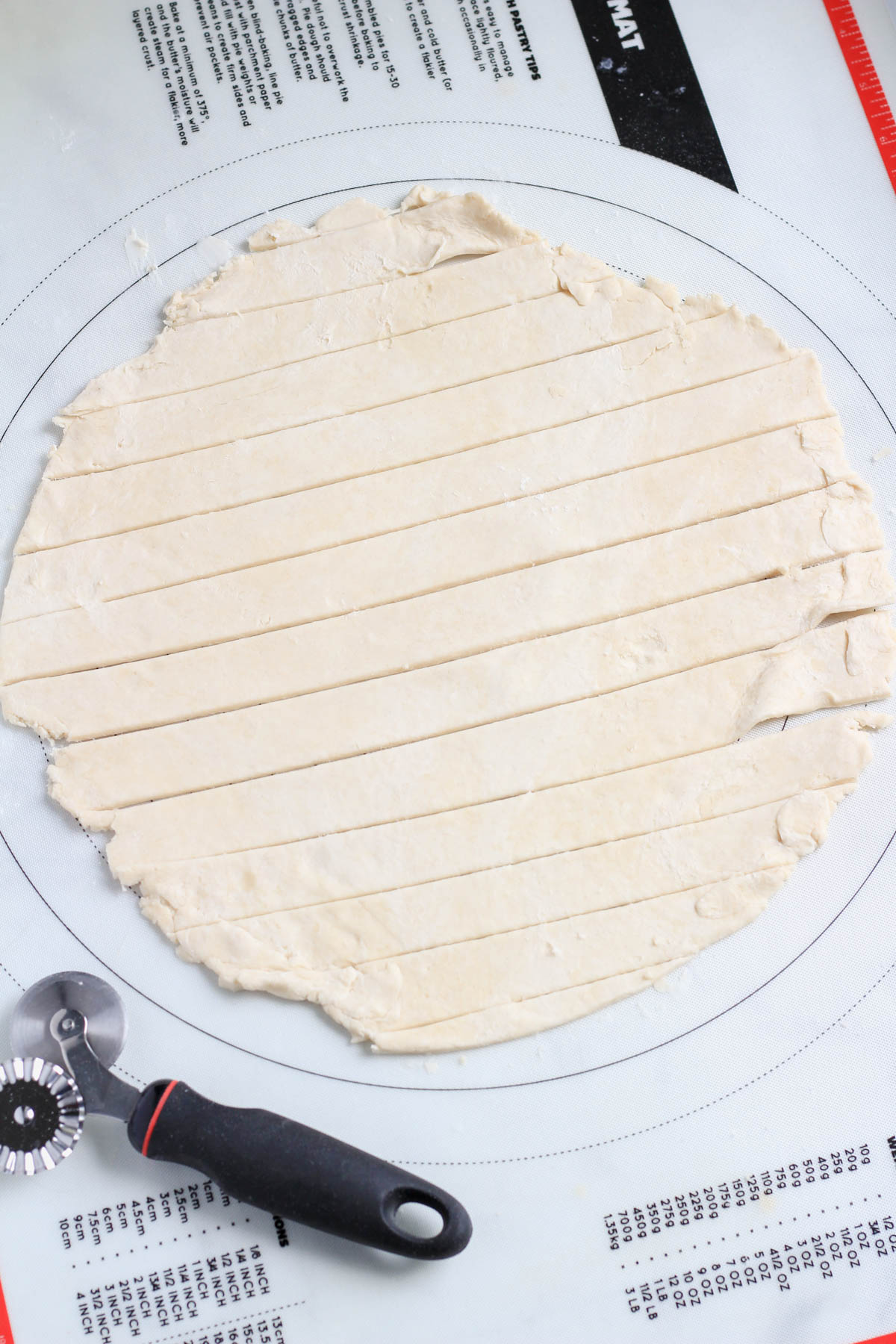 A pastry mat with a 12-inch round of vegan all butter pie crust and a pie cutter in the bottom left.