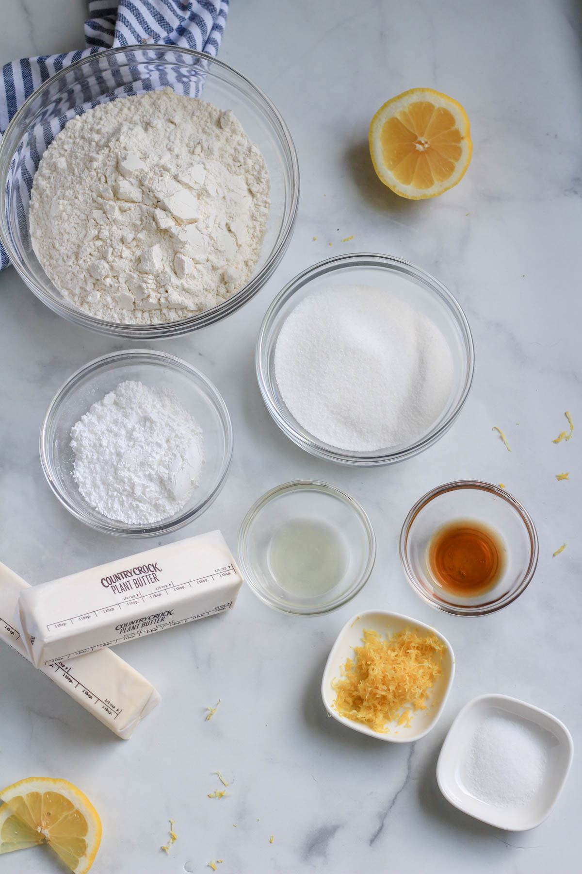 Ingredients for lemon shortbread on a white counter with a blue and white striped towel.