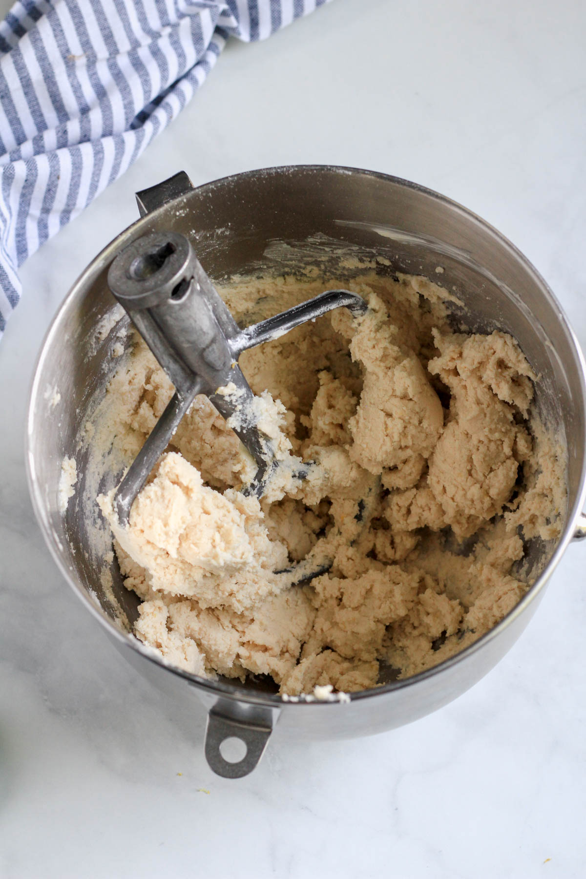 Lemon shortbread cookie dough in a silver bowl with a paddle attachment.