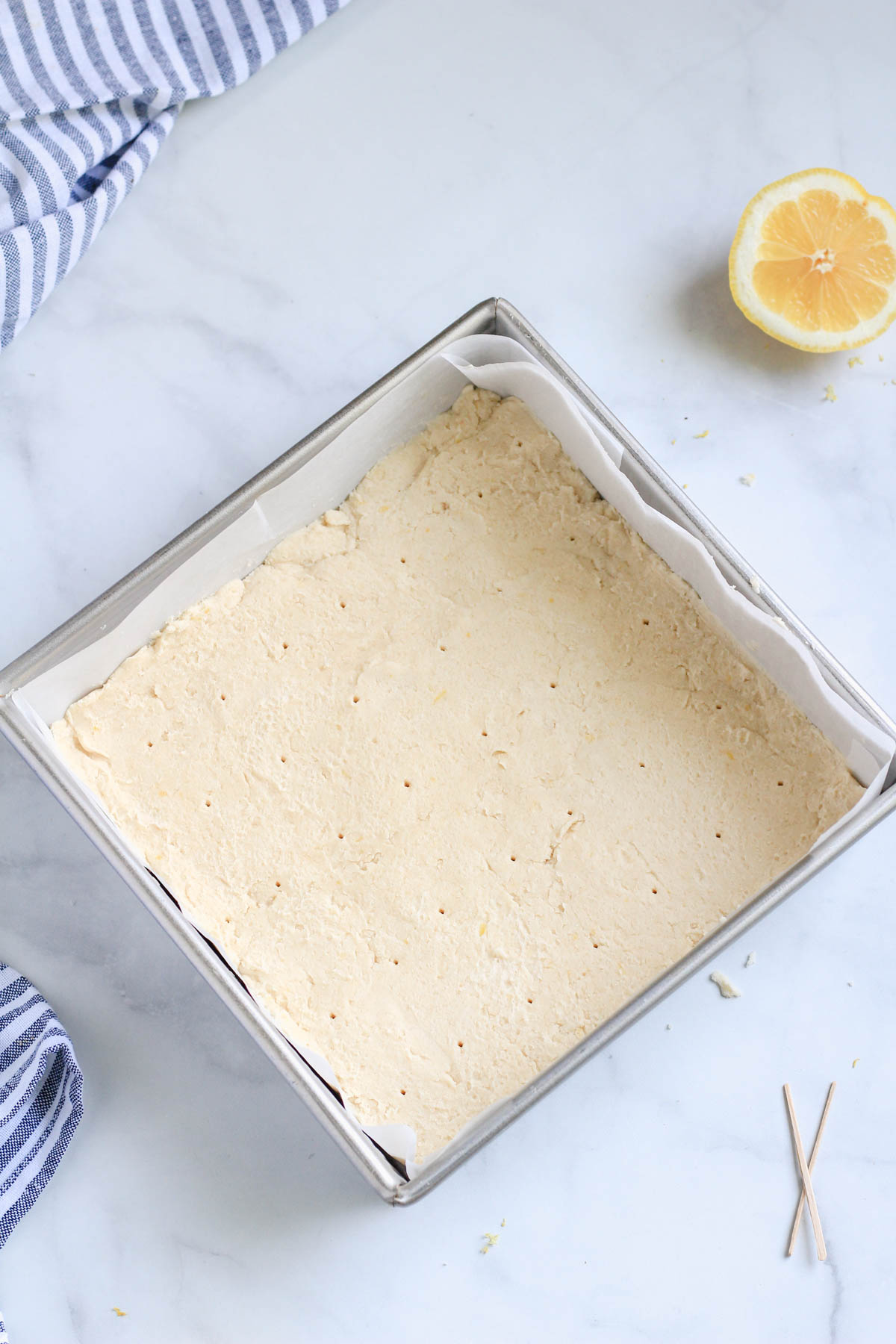 A square baking dish with vegan lemon shortbread dough after being pricked, before being baked.