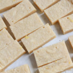 A close up of lemon shortbread cookie after being cut on parchment paper.