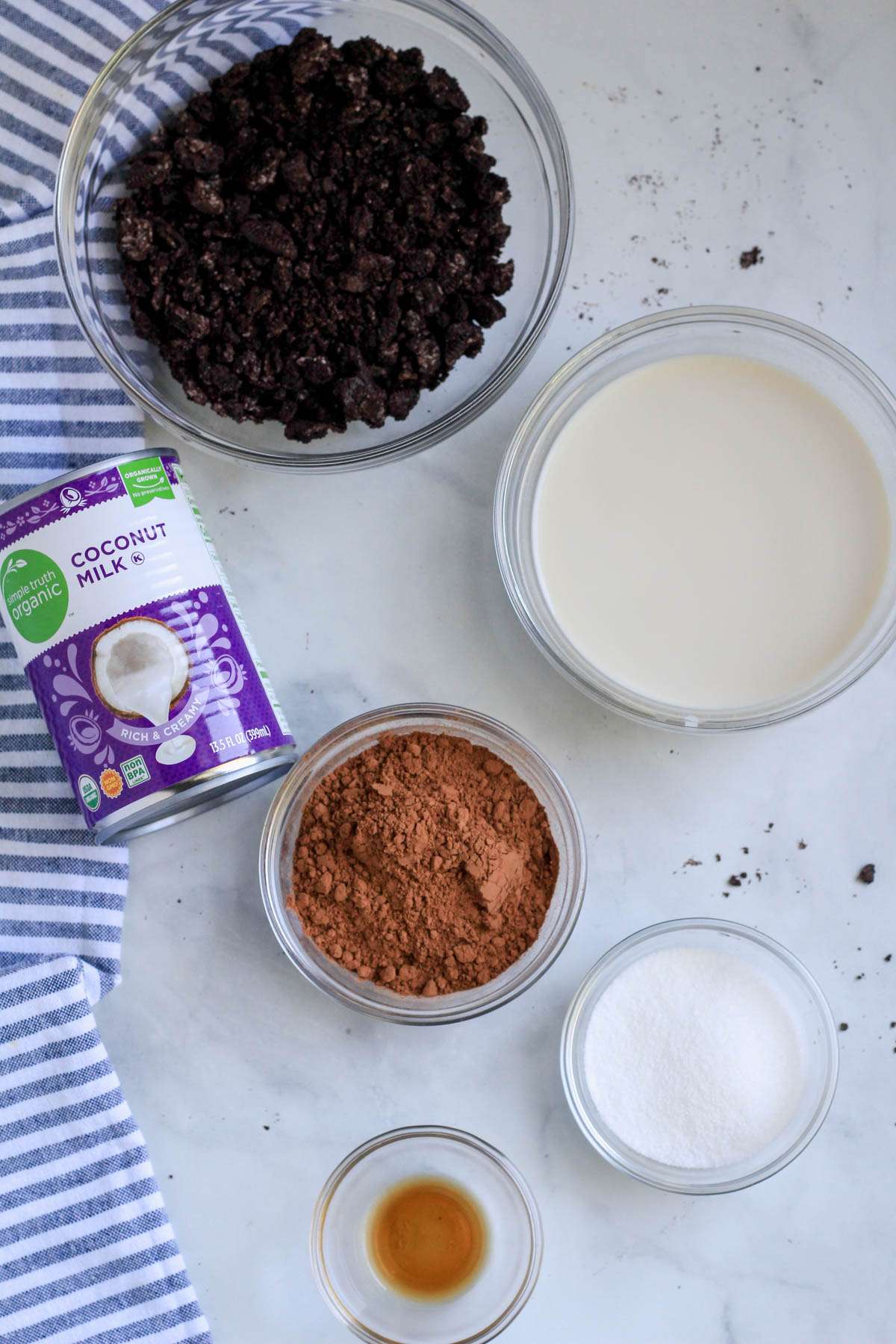 Ingredients for oreo fudgesicles on a white counter with a blue and white striped dish towel to the left.