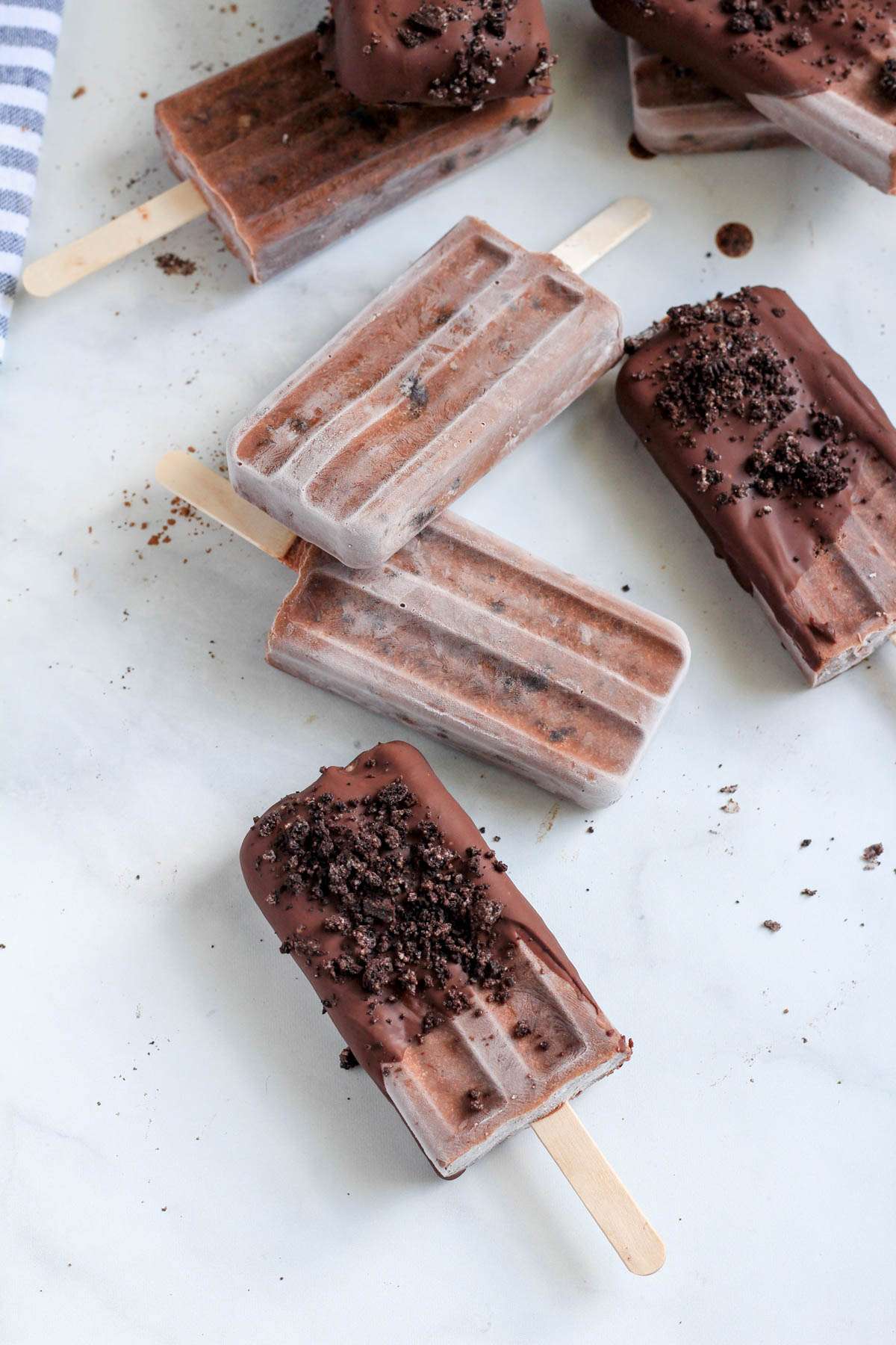 A chocolate dipped Oreo fudgesicle in front of 7 other Oreo fudgesicles on a white counter.