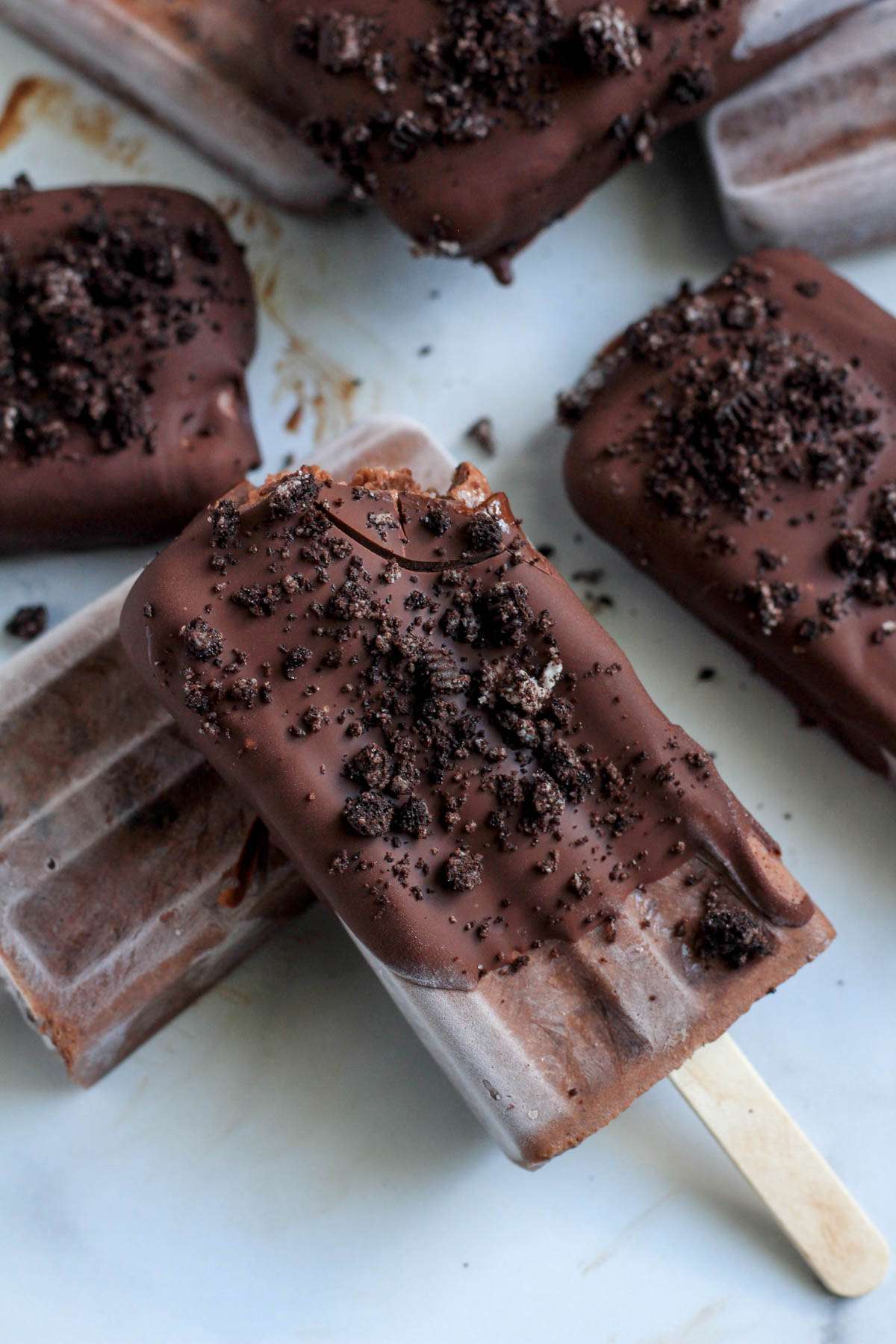 A close up of a chocolate dipped Oreo fudgesicle with a bite taken out.