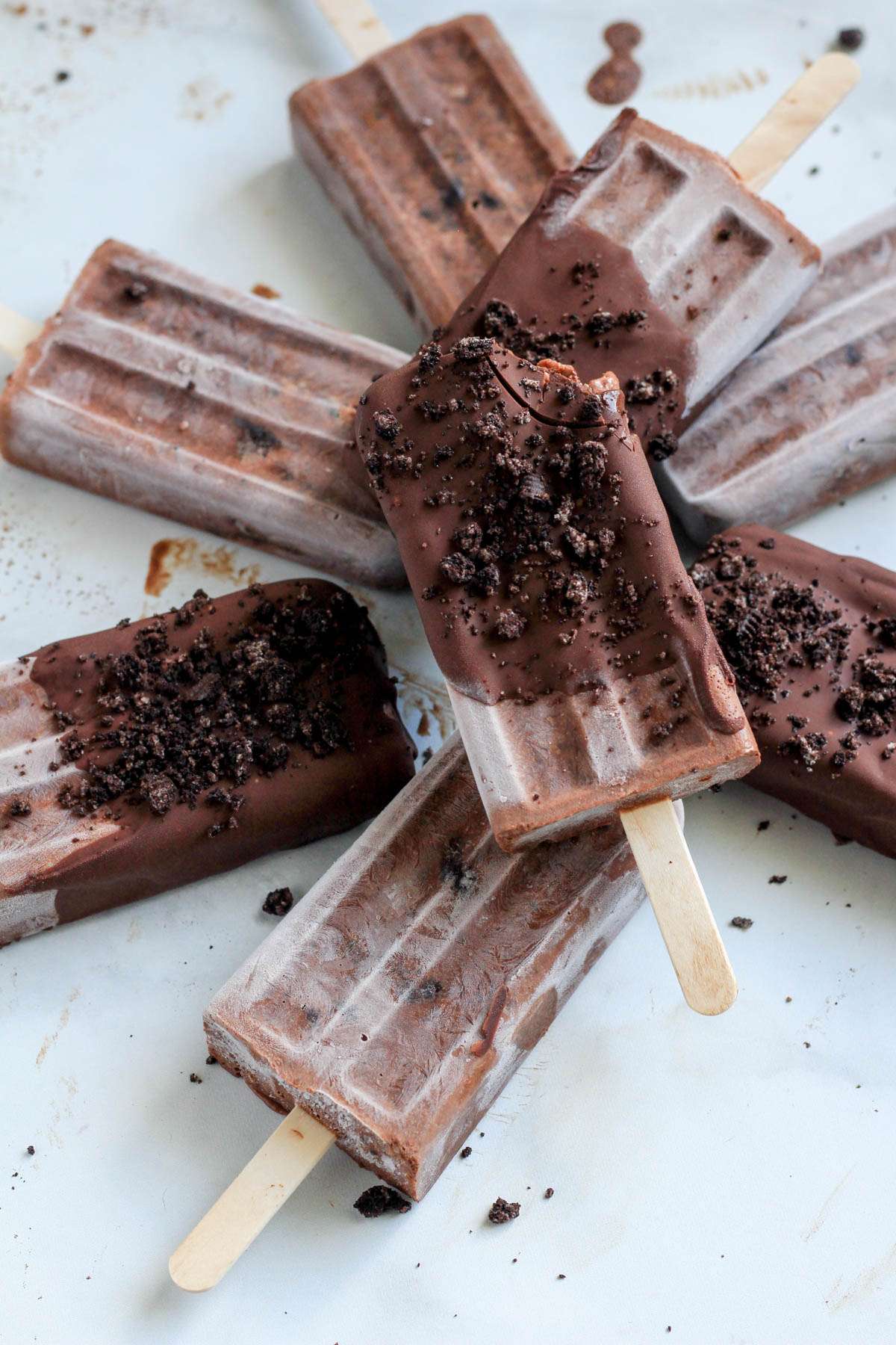 A pile of chocolate Oreo fudgesicles on a white counter with a bite out of the top popsicle.