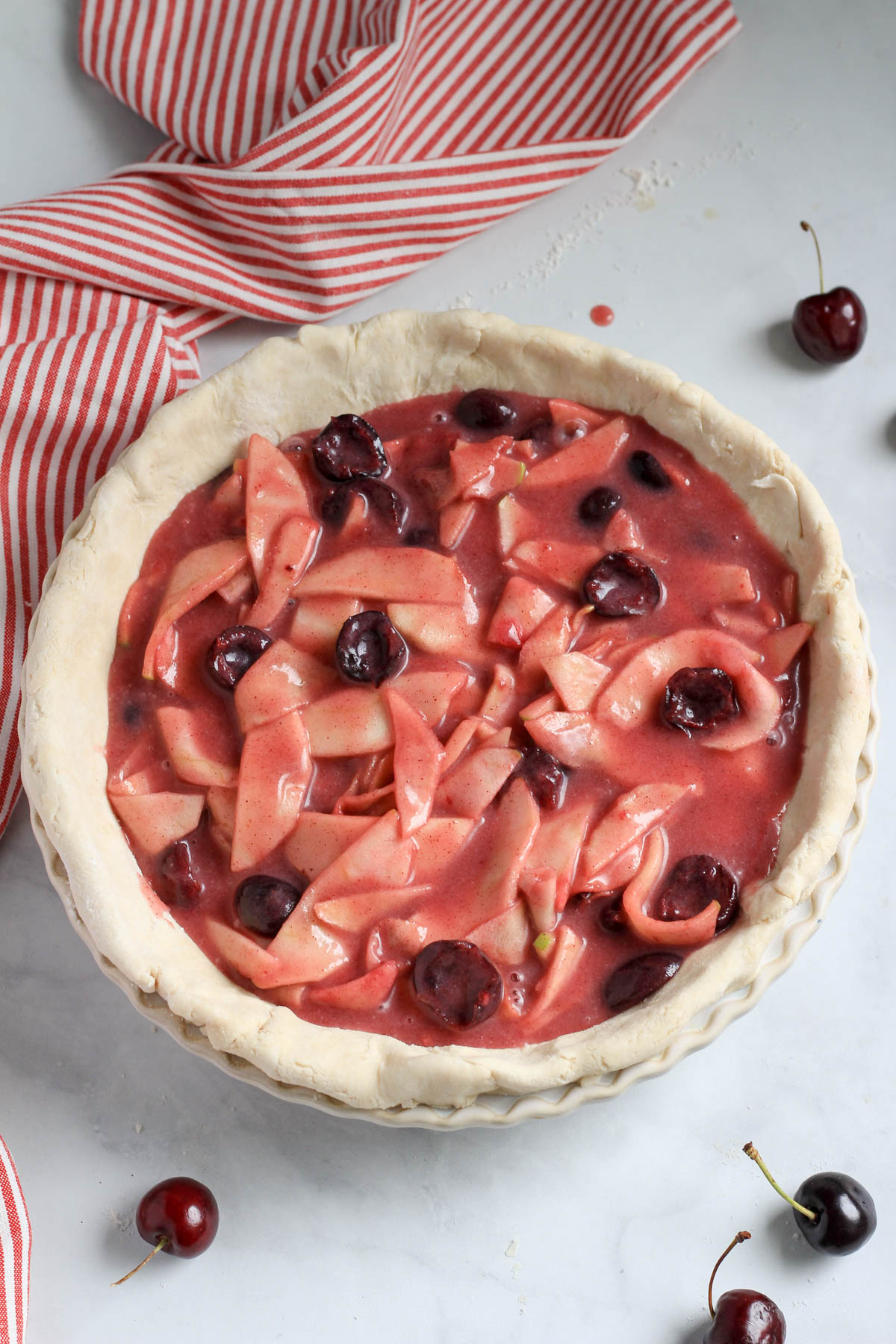 Cherry apple pie filling in the pie crust with a red and white striped dish towel to the left.