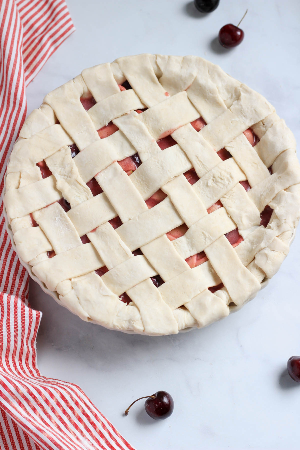 A vegan cherry apple pie with a lattice top before being brushed and topped with sugar.