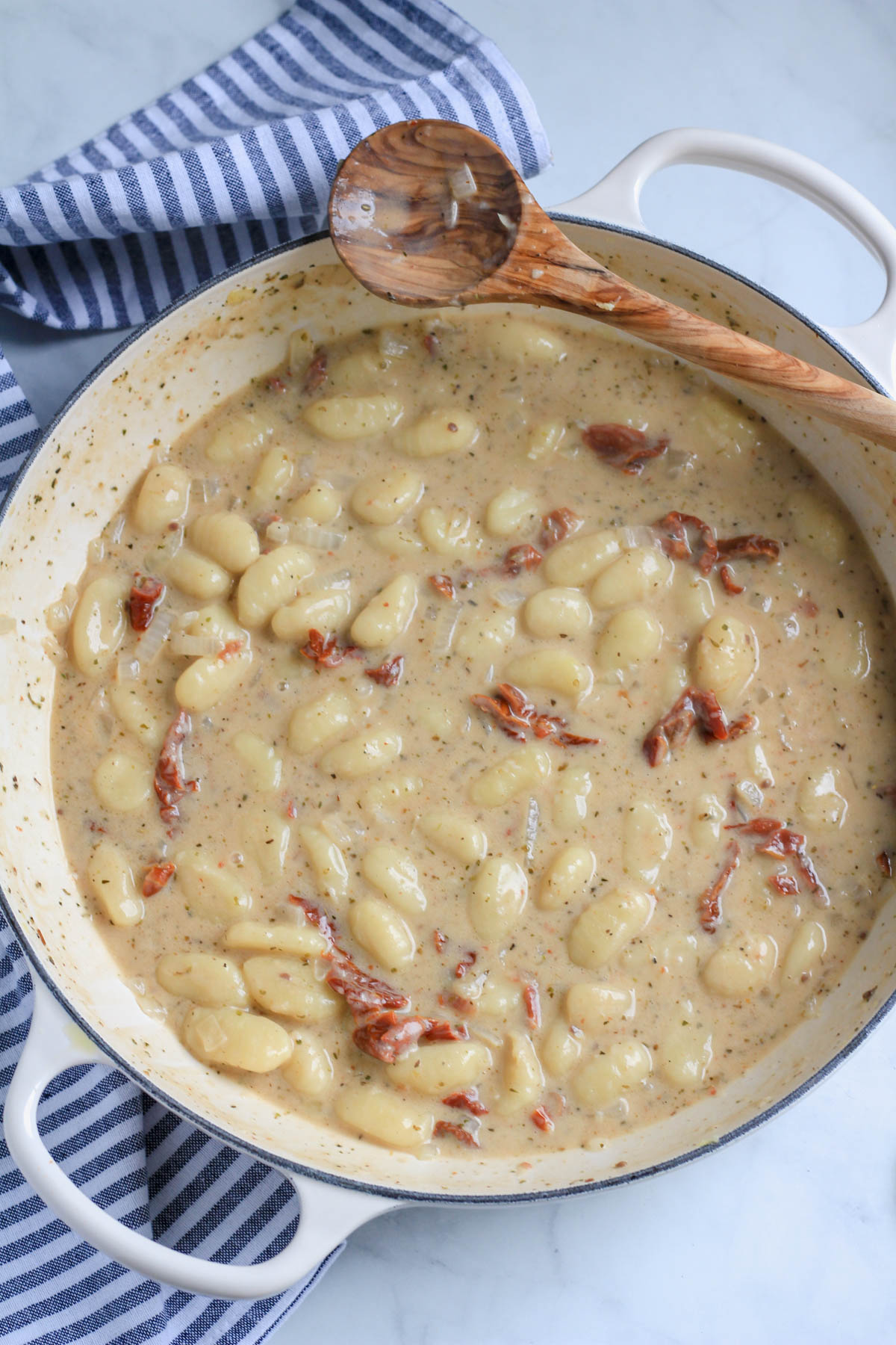 A white skillet with the gnocchi and creamy sun dried tomato sauce after thickening.