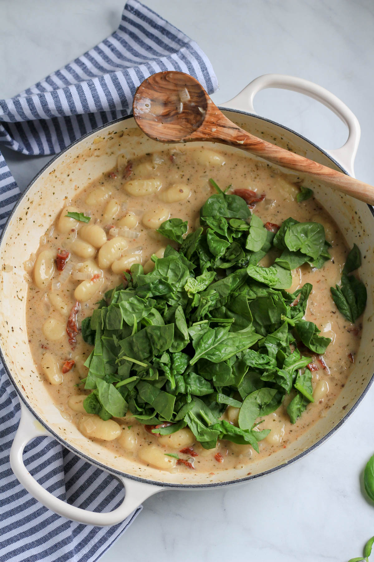 A white skillet with vegan gnocchi topped with spinach before wilting.