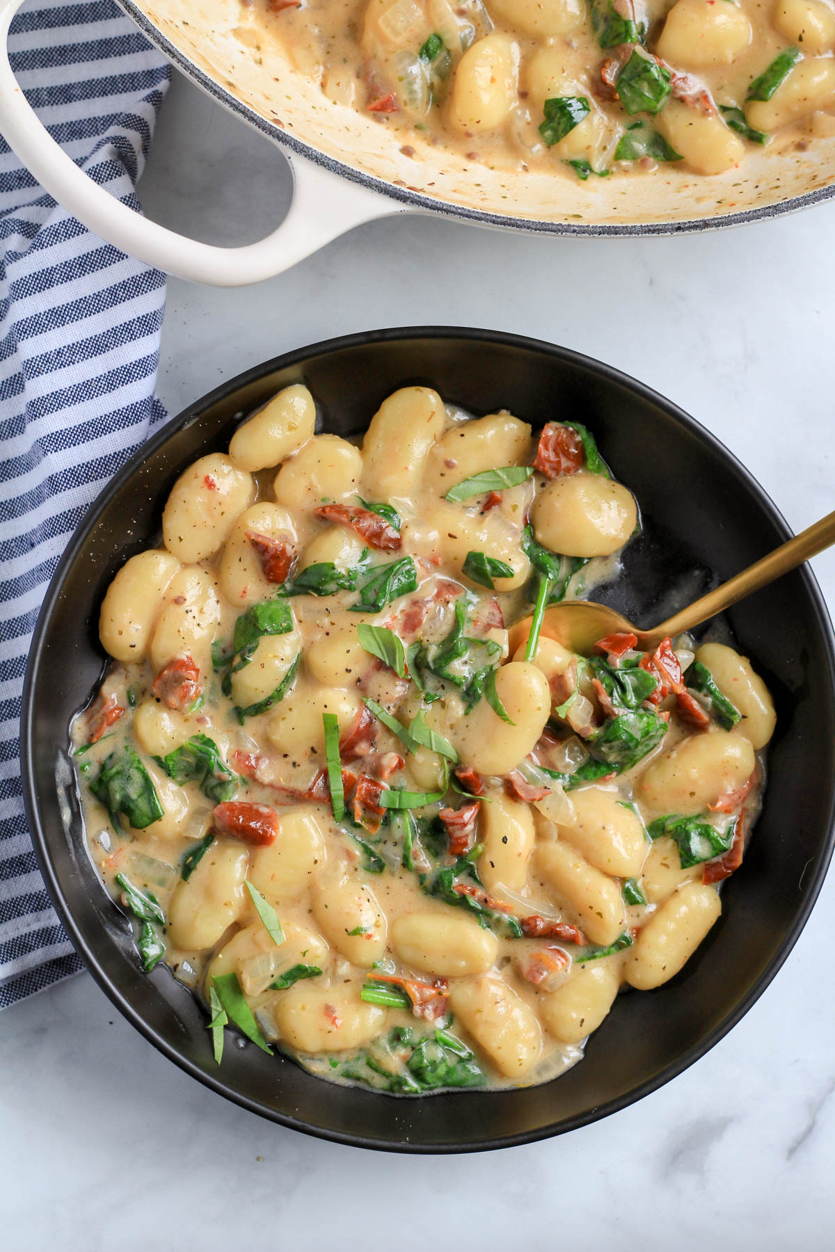 A top down photo of creamy vegan gnocchi with a gold spoon on a white counter.