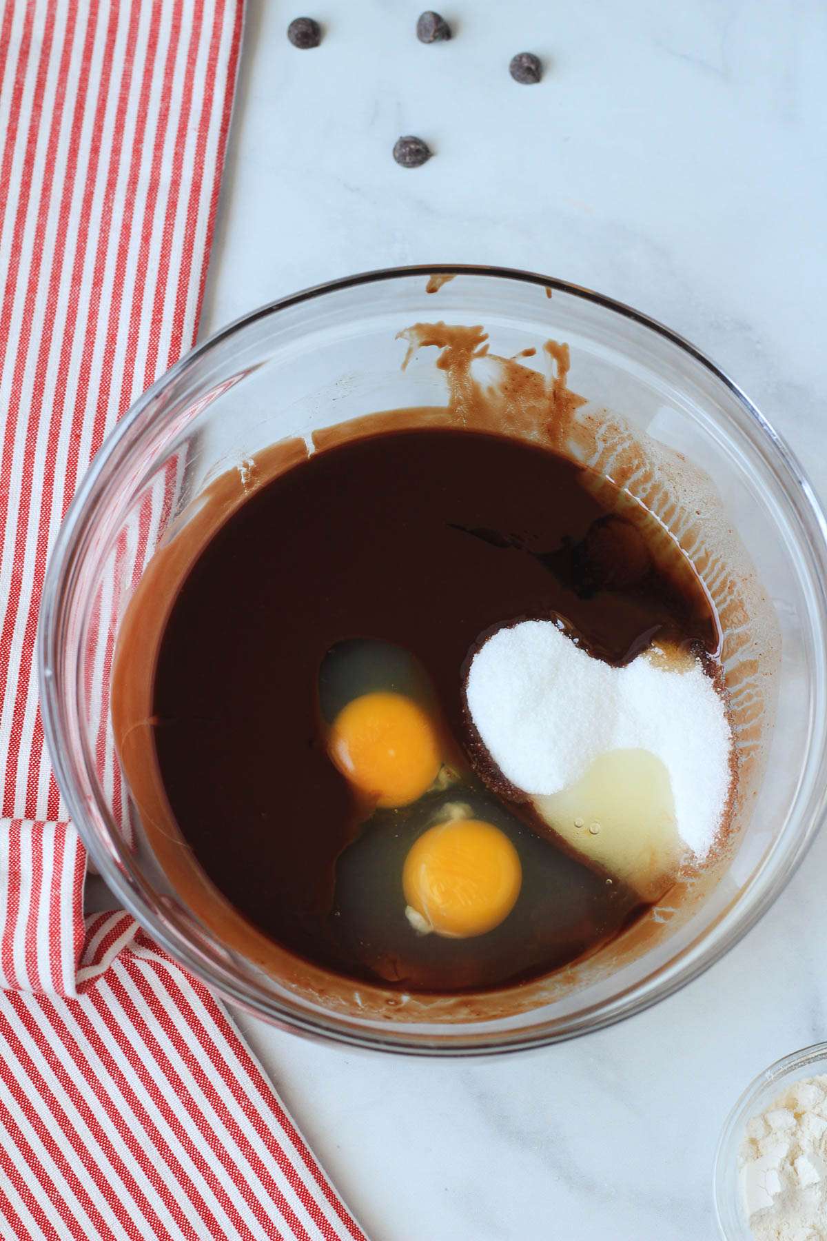 Eggs, sugar, and vanilla added to the melted vegan butter and dairy-free chocolate in a glass mixing bowl.