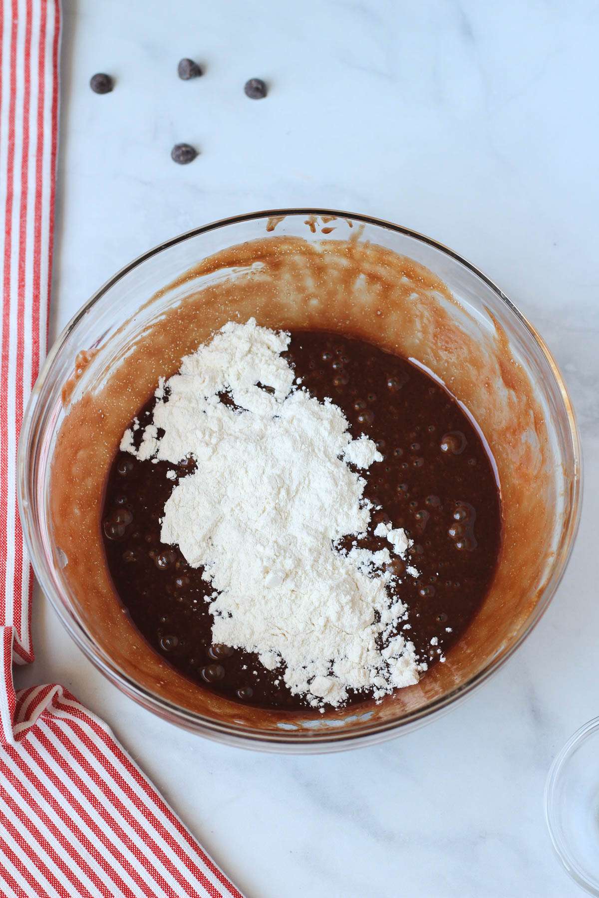 A glass mixing bowl with the chocolate lava cake batter topped with flour before folding in.