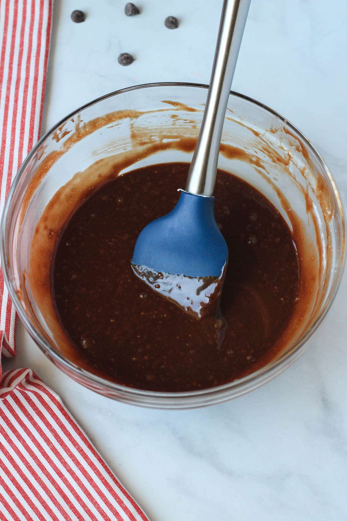 A glass mixing bowl with chocolate lava cake batter and a blue spatula.
