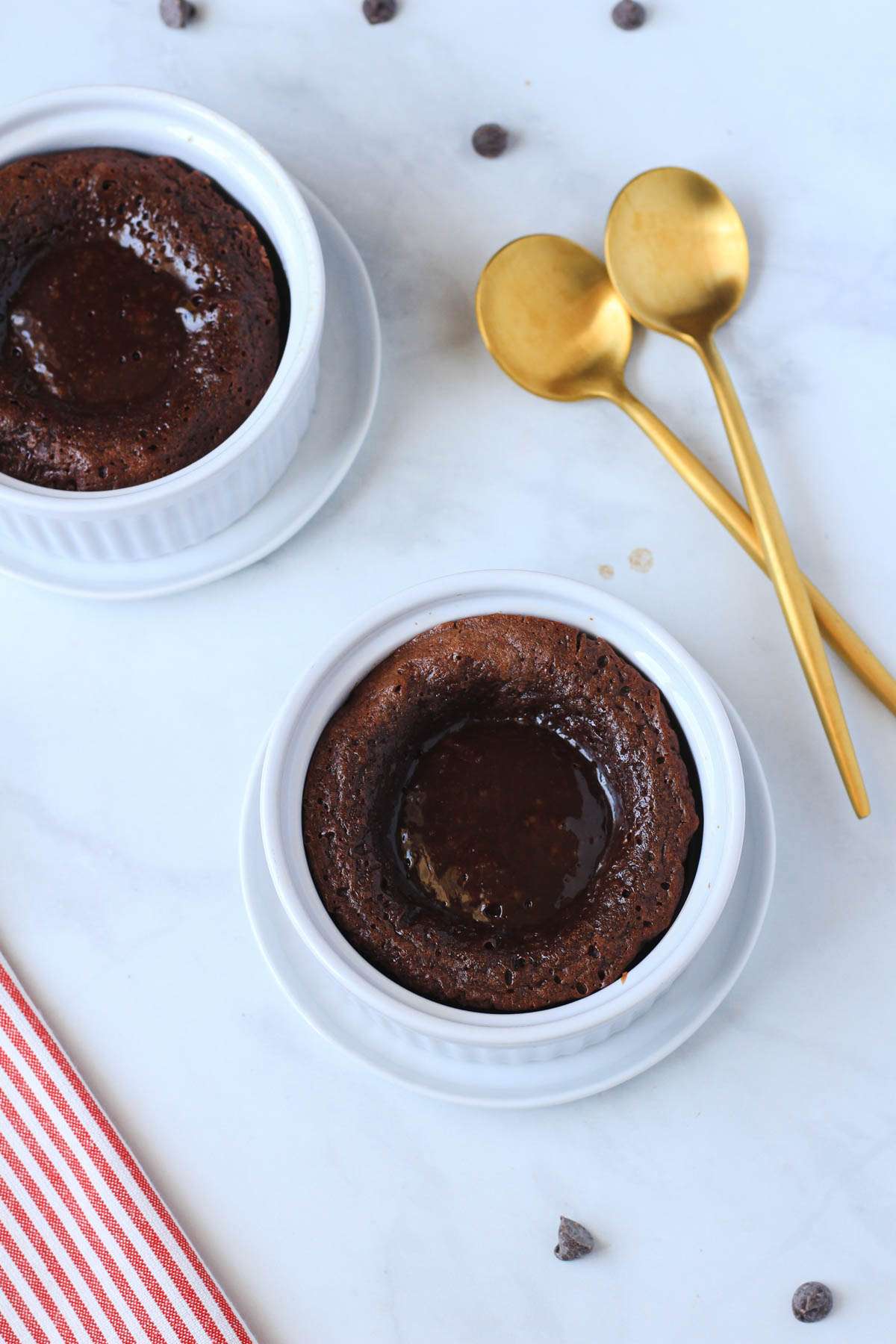 Molten chocolate lava cakes on a white counter with gold spoons to the right.