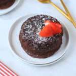 A molten chocolate lava cake on a white plate topped with powdered sugar and sliced strawberries.