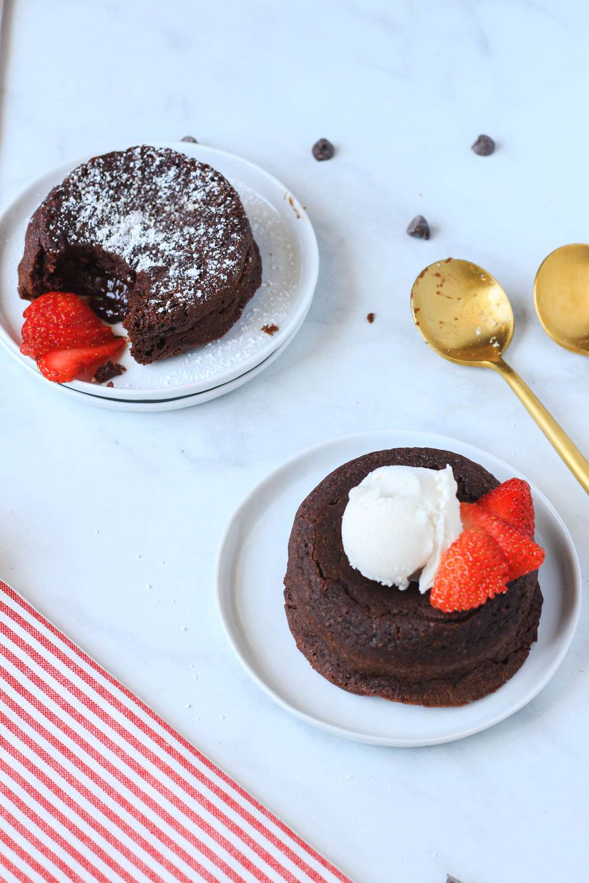 Two chocolate lava cakes on white plates one in the back right with powdered sugar and one in the front right with a scoop of dairy-free ice cream.