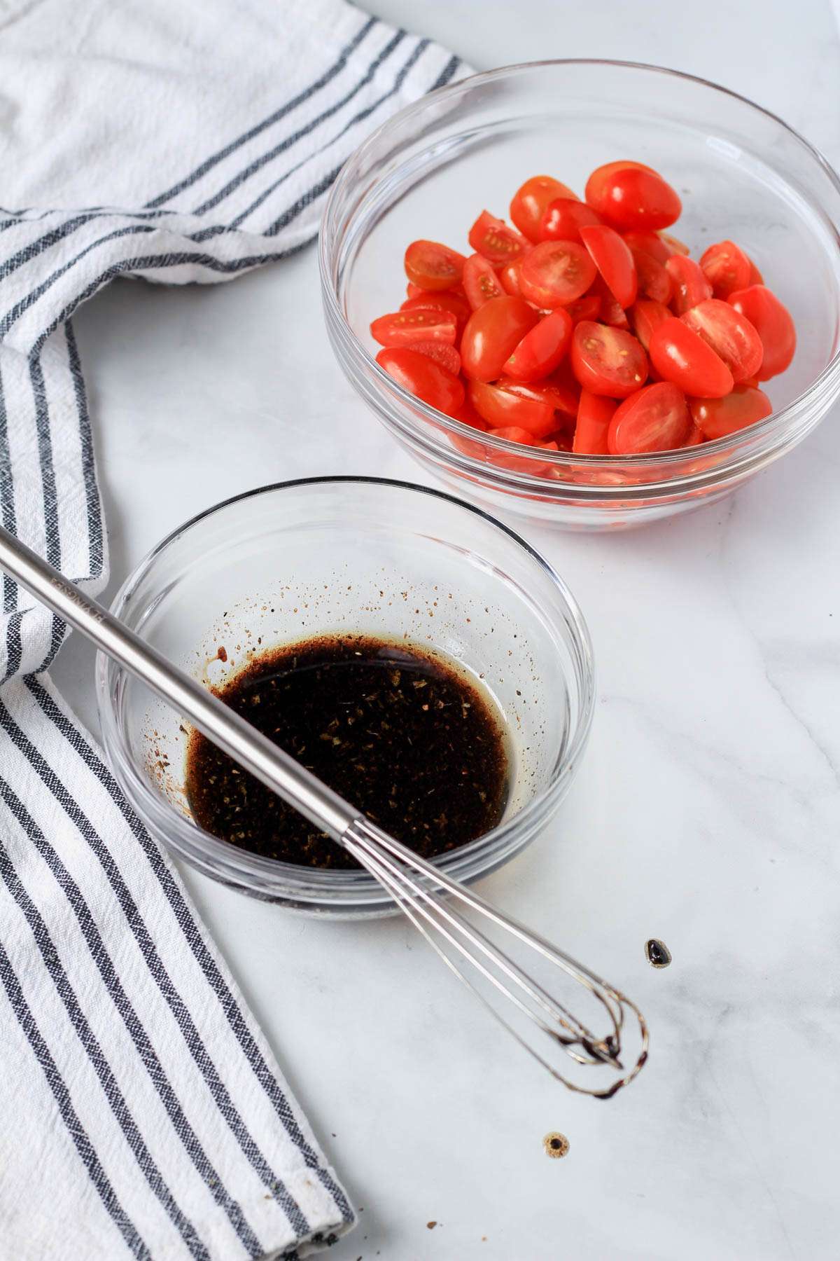 A bowl with the balsamic marinade and another bowl in the back with chopped tomatoes.