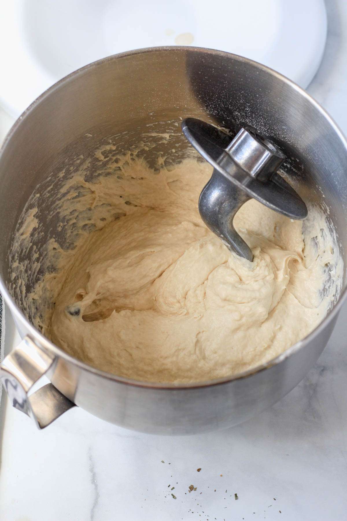 Focaccia dough in a silver bowl with a dough hook attachment.