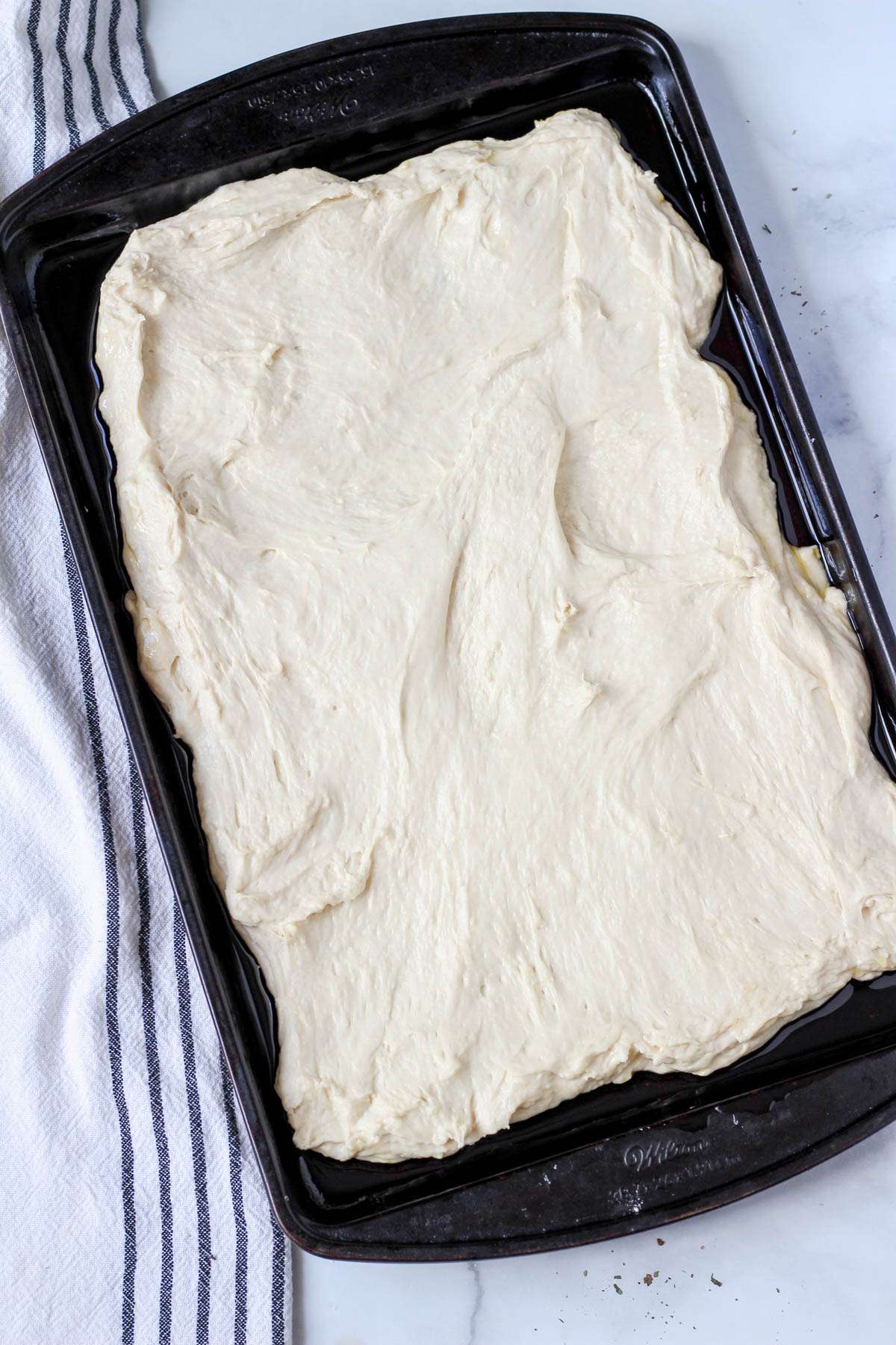 A rimmed baking sheet topped with focaccia dough after spreading out.