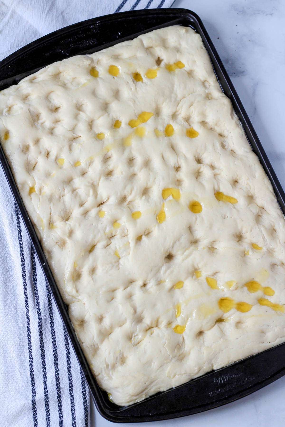 Focaccia dough with holes poked in and topped with a drizzle of olive oil.