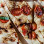 A triangle shaped slice of focaccia with balsamic marinated tomatoes on a cutting board.
