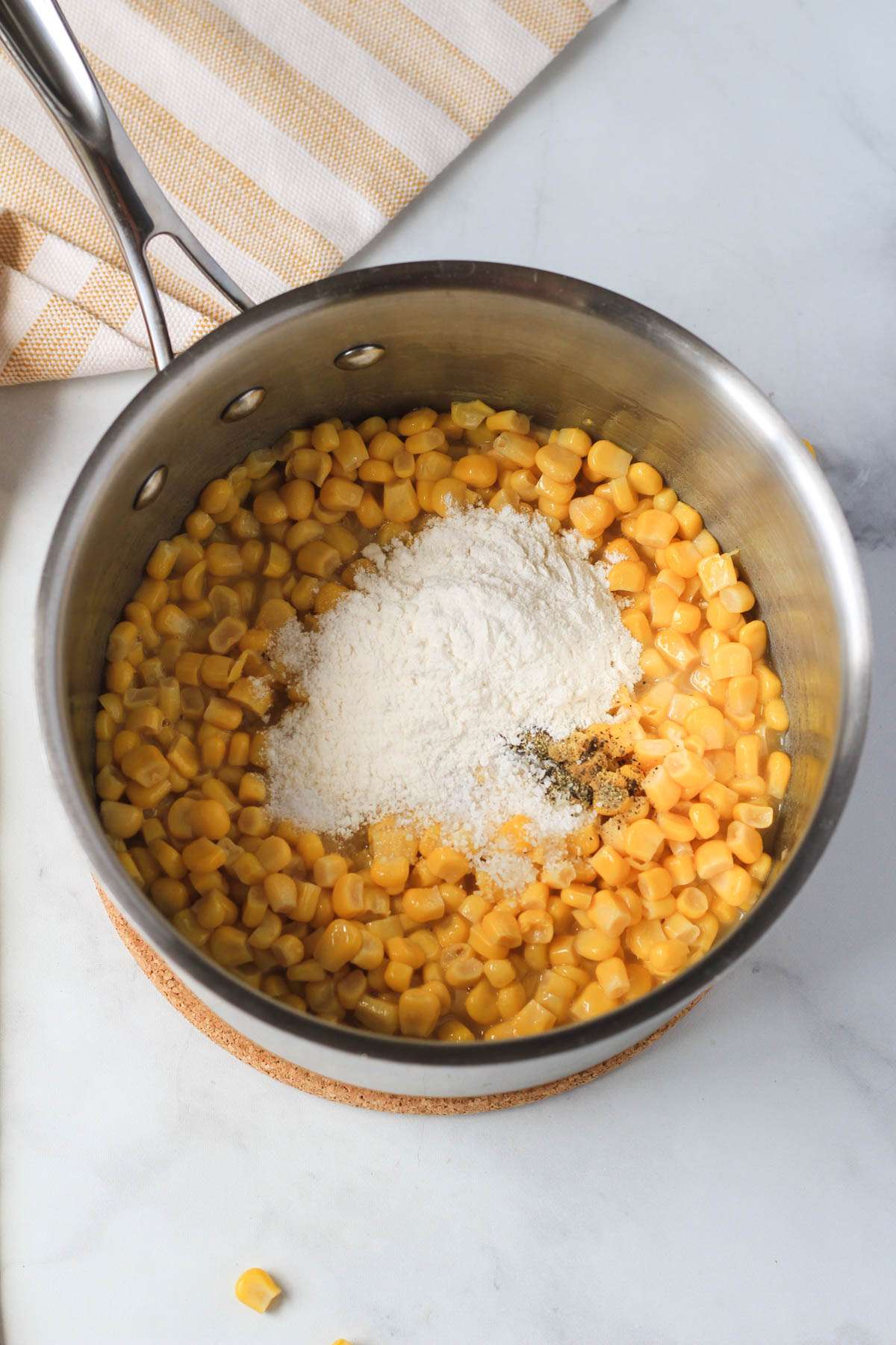 A silver sauce pan with corn, flour, salt, pepper, and sugar.