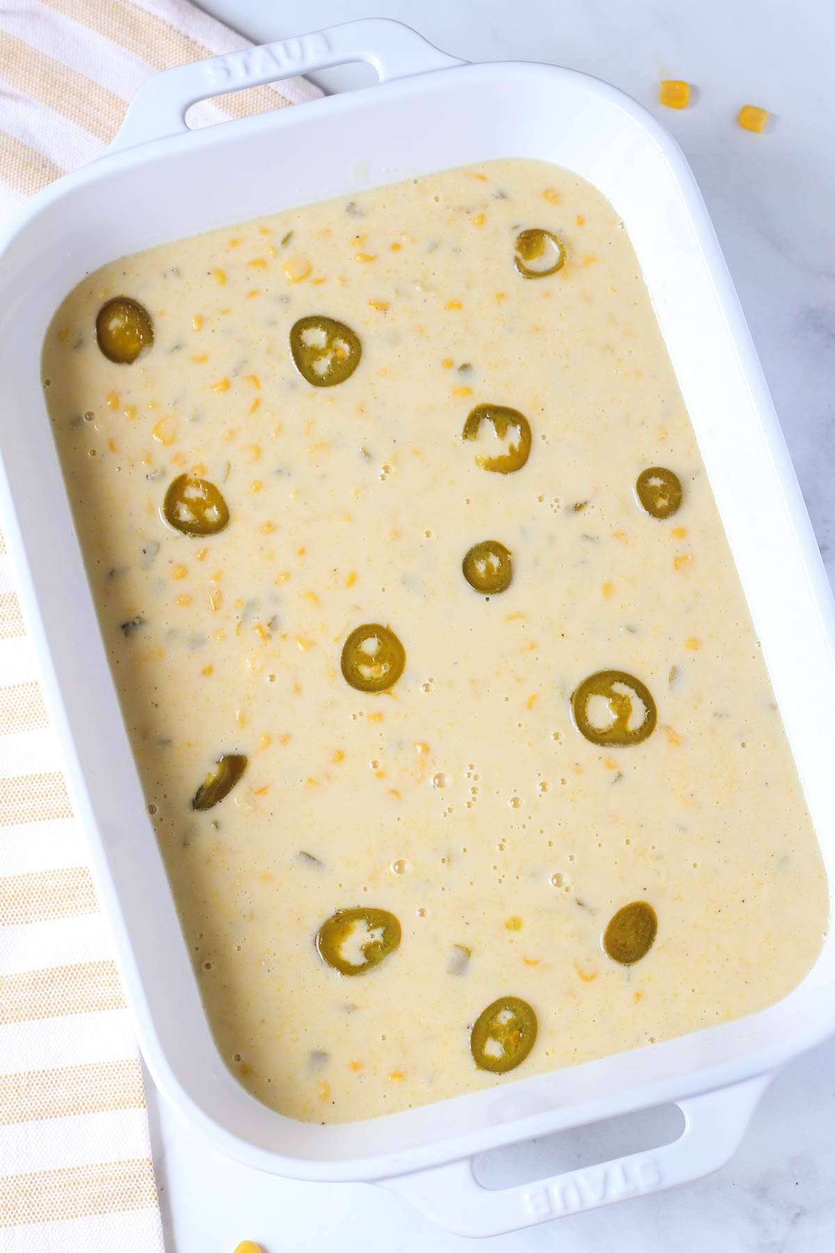 Pickled jalapeños top the jalapeño corn casserole in a white baking dish.