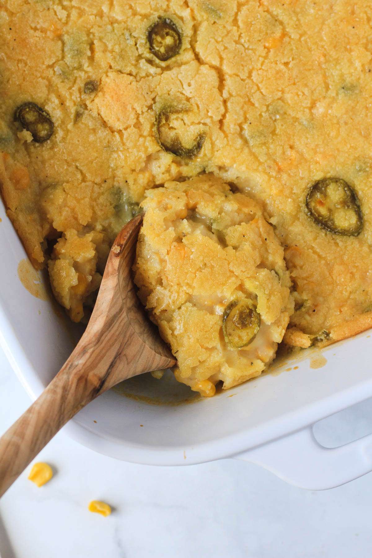 A wooden spoon in the corn casserole with a scoop of casserole on the spoon.