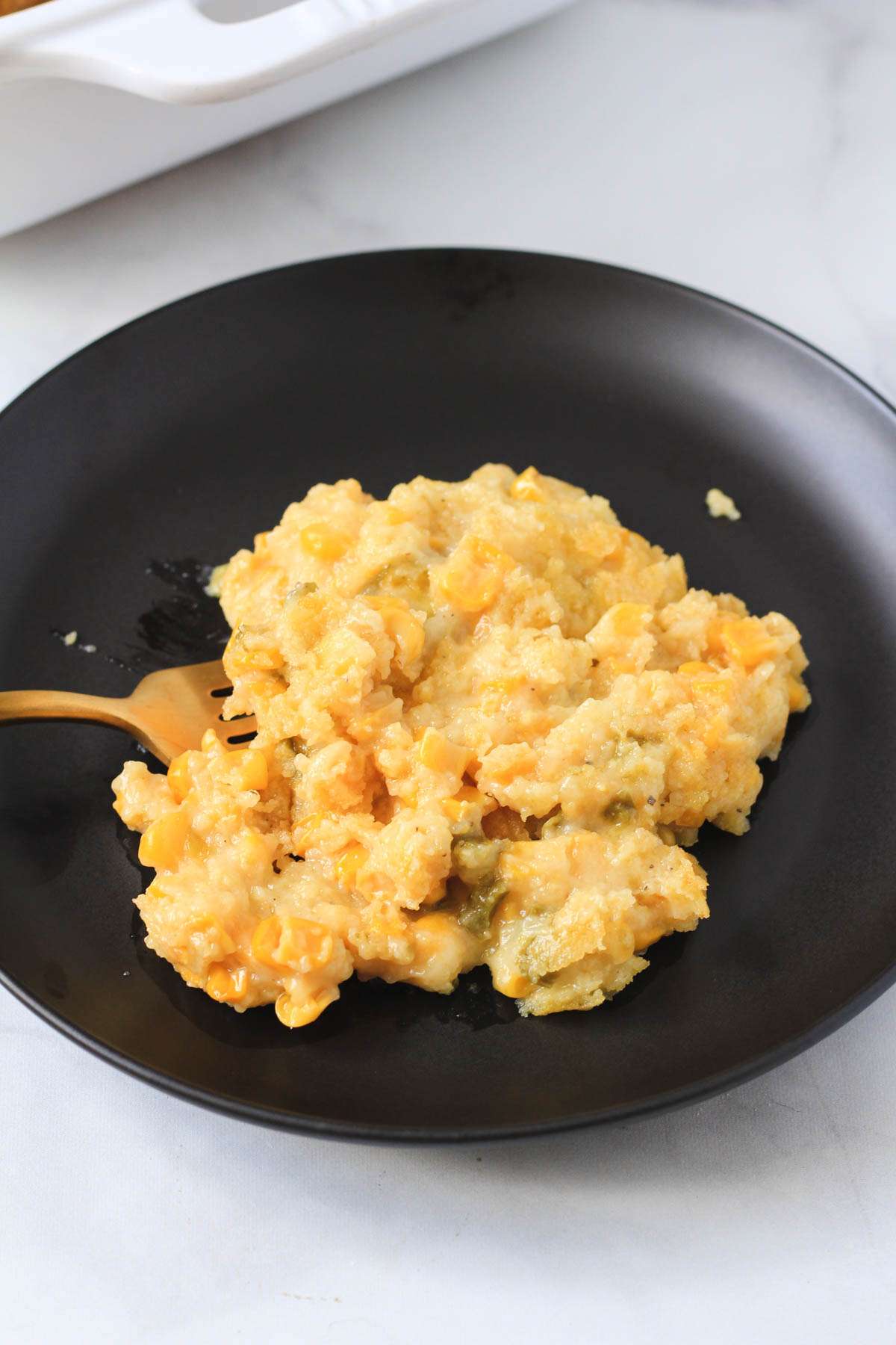 A black plate with a scoop of jalapeño corn casserole with a gold fork on the left side of the plate.