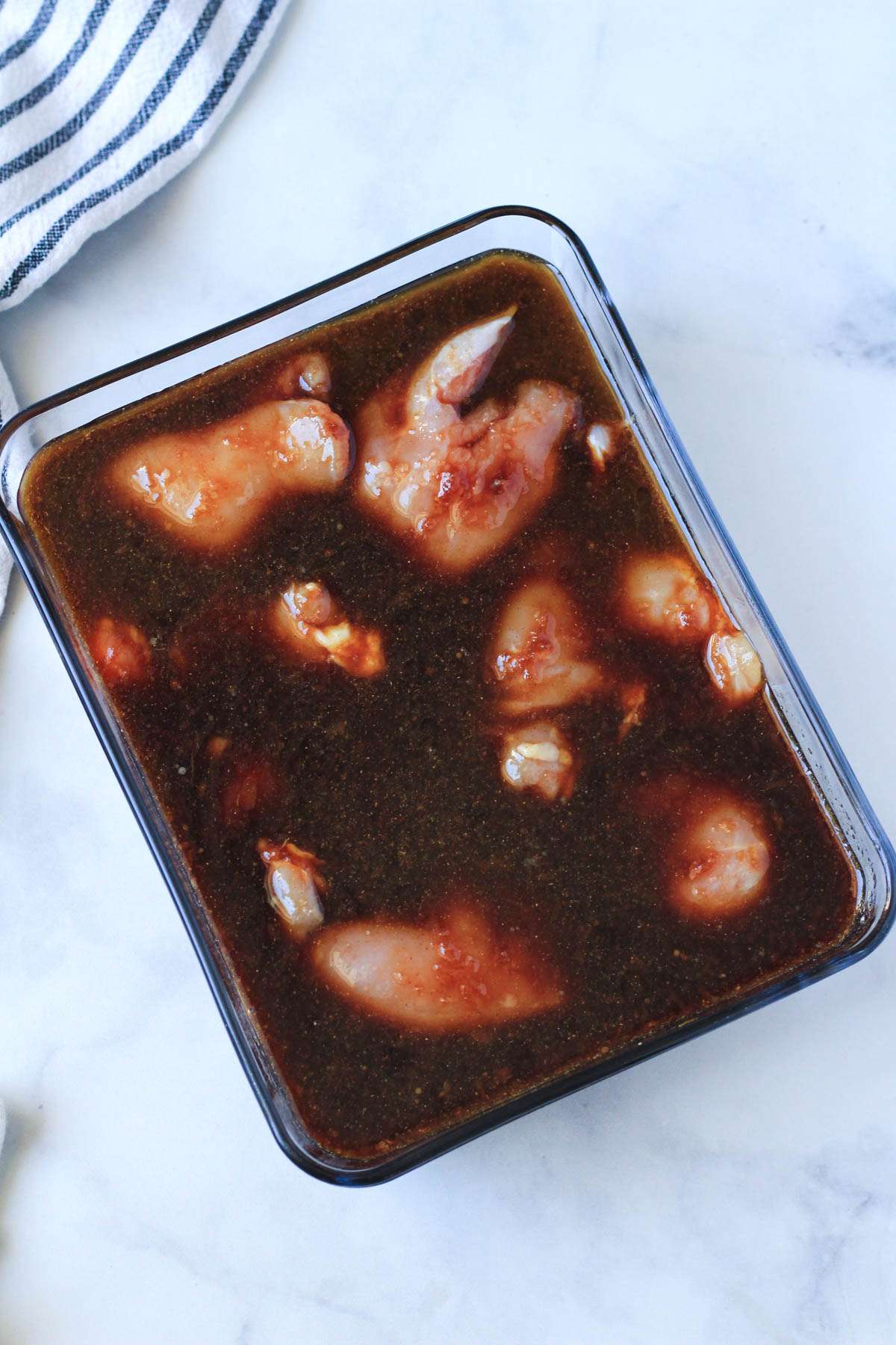 A glass dish filled with chicken thighs and the soy marinade.