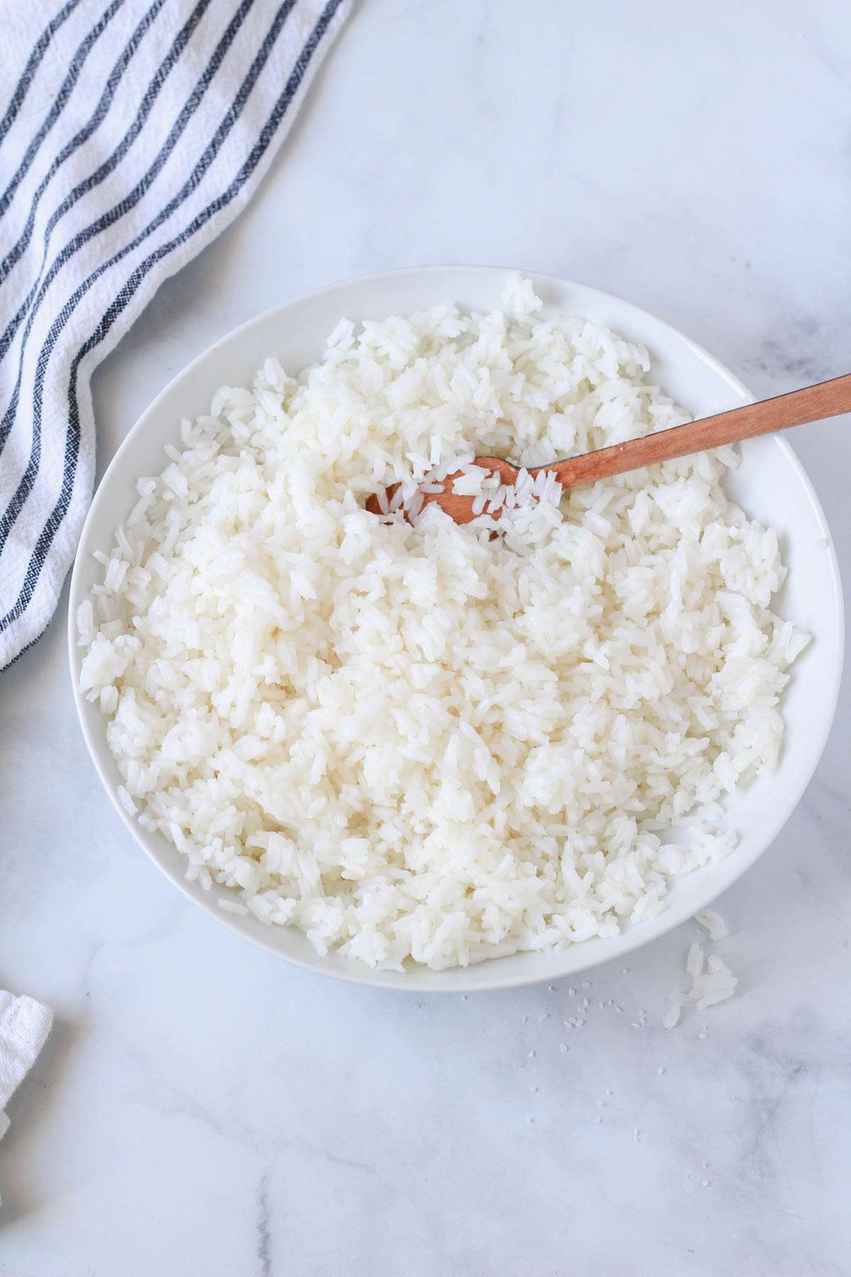 A white bowl with long grain sticky rice and a wooden spatula.