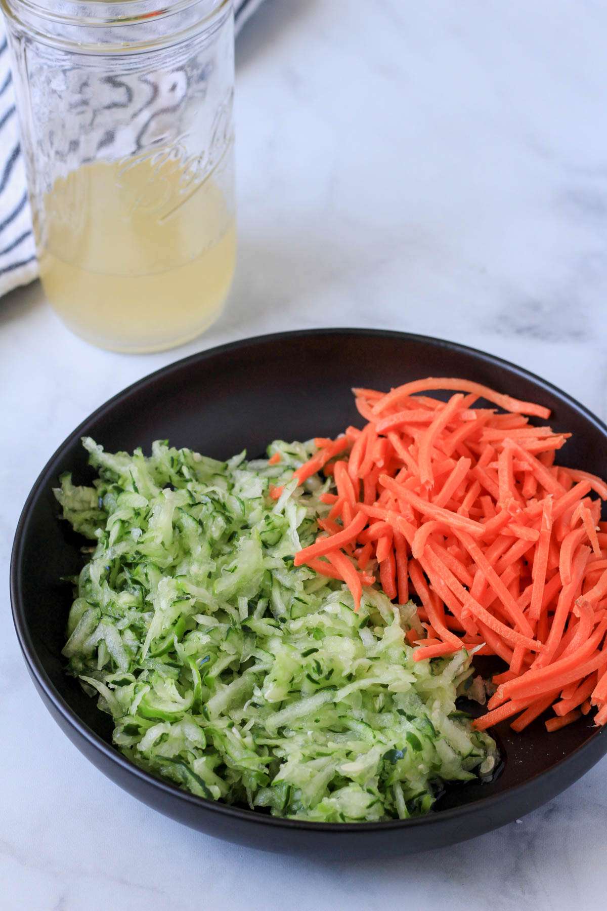 A close up of shredded carrots and cucumbers on a black plate.