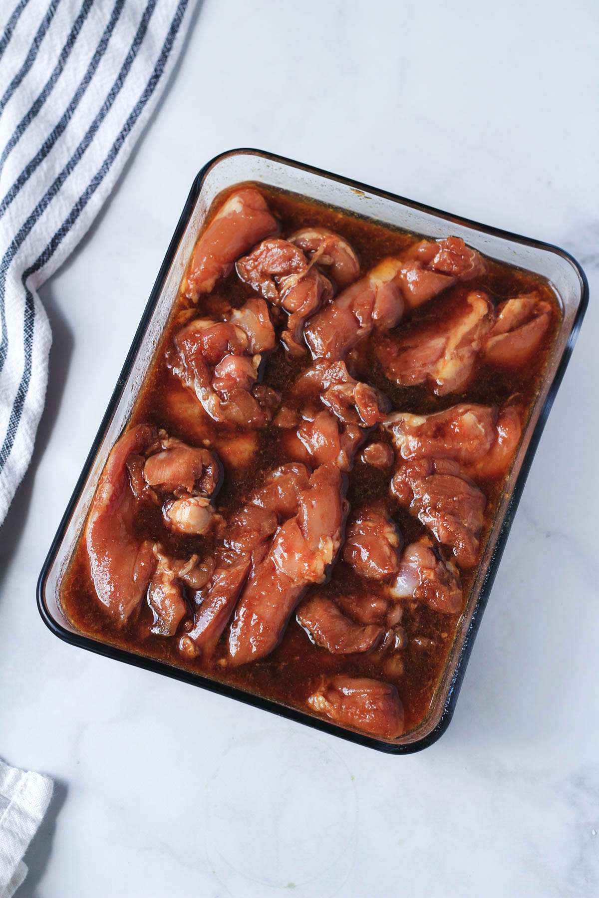 A shallow glass dish with marinated chicken thighs before grilling.