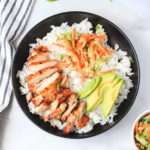 A close up of a soy marinated chicken thigh bowl in a black bowl on a white counter.