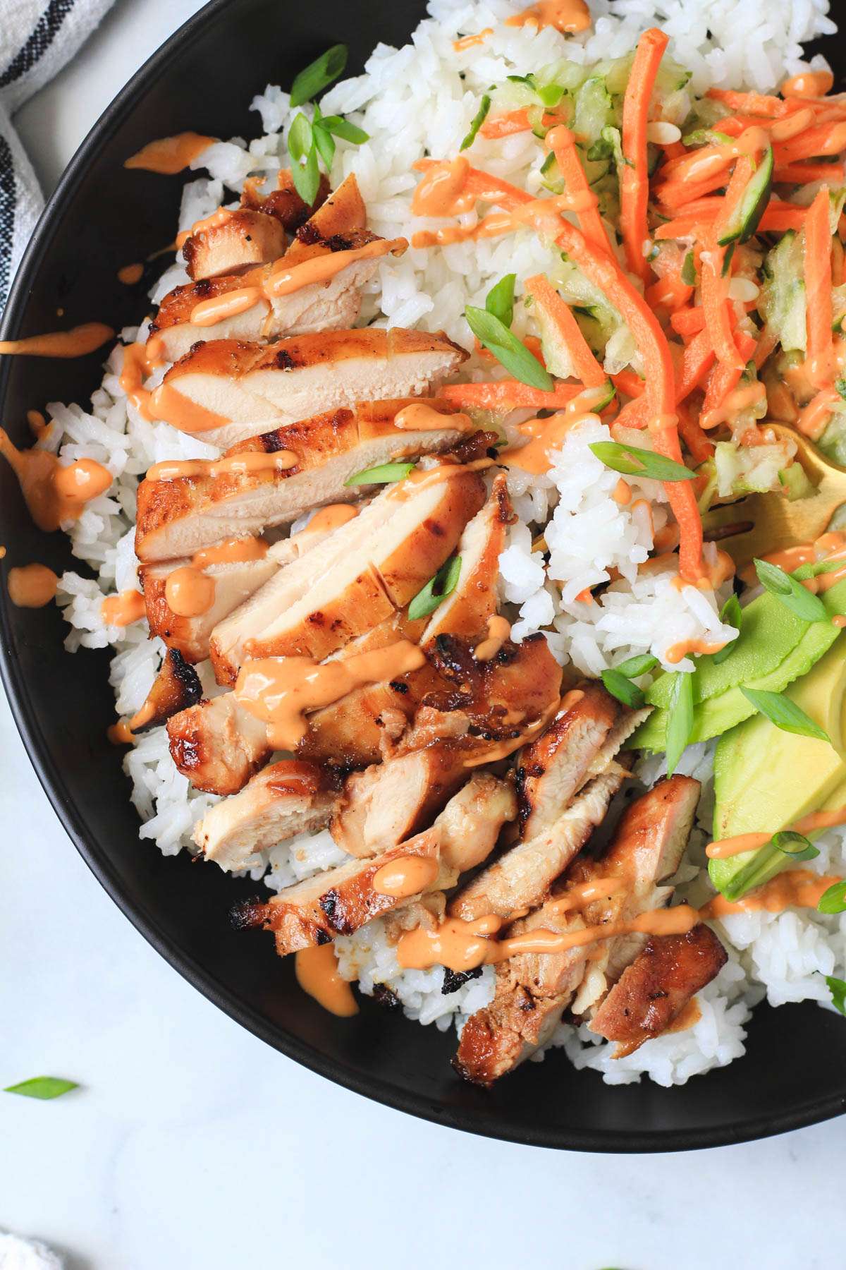 A close up of the soy-marinated chicken thigh bowl in a black bowl on sticky rice.