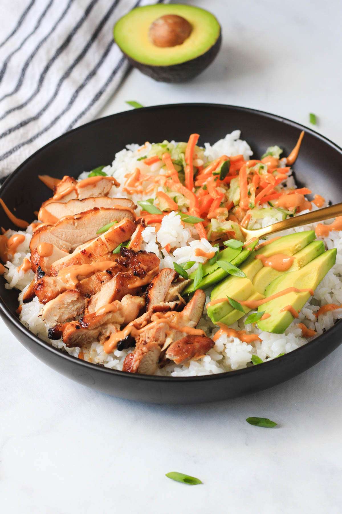 A rice bowl with soy marinated chicken thighs in a black bowl with a gold fork on a white counter.